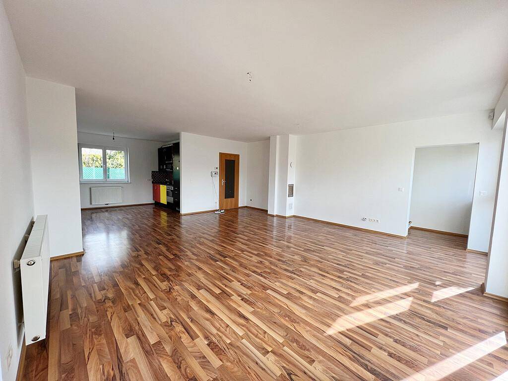 Weitläufiger Wohnbereich mit hellem Laminatboden und offener Gestaltung, ideal für flexible Einrichtung.