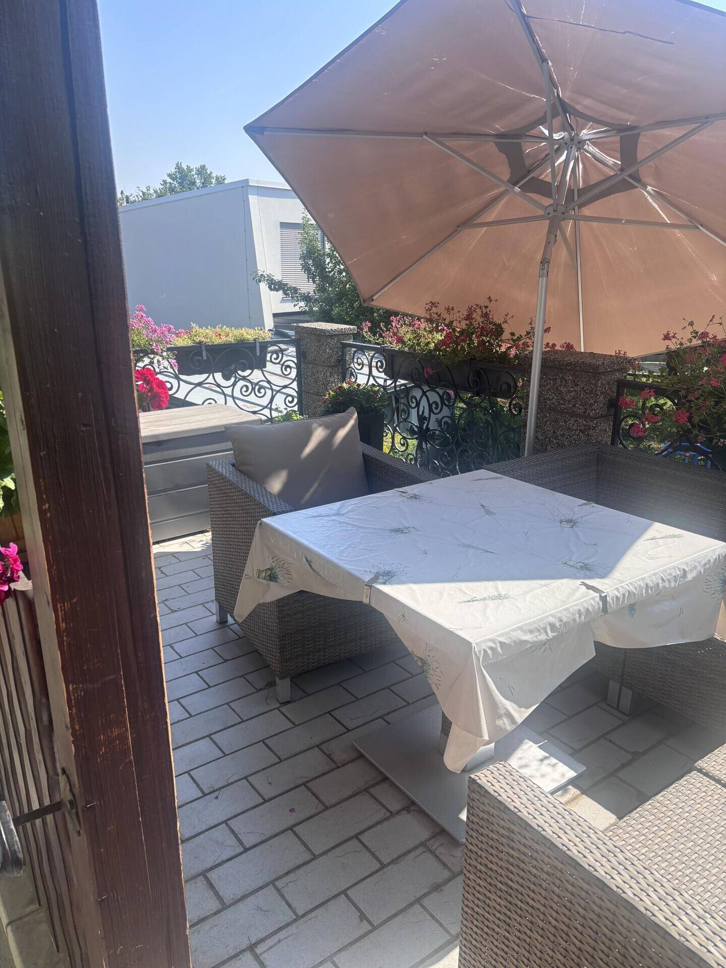 Gemütliche Terrasse mit Pflastersteinen, Gartenmöbeln und einem großen Sonnenschirm, umgeben von Blumen.