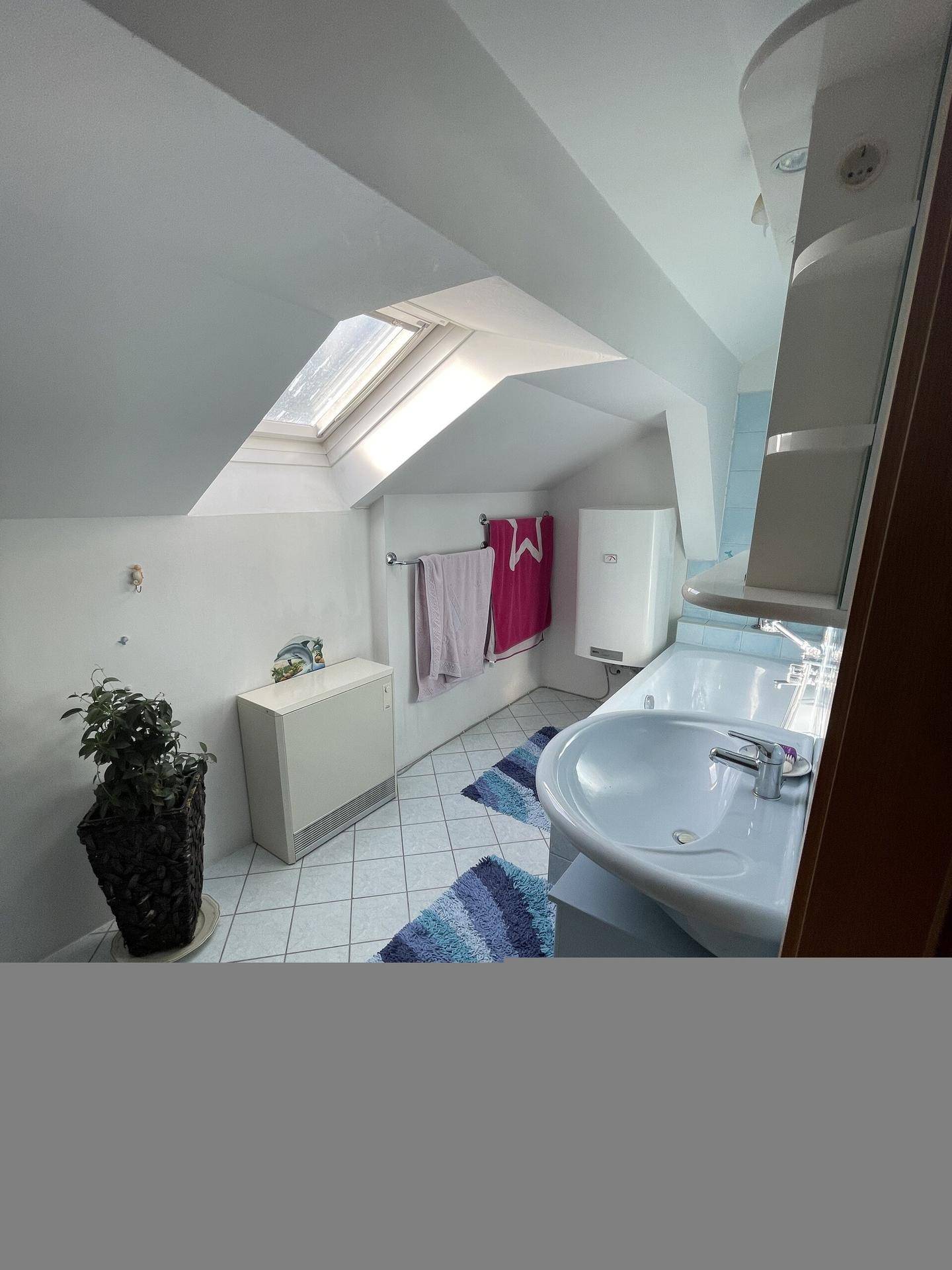 Dachgeschoss-Badezimmer mit Dachfenster, Waschtisch und blauen Akzenten.