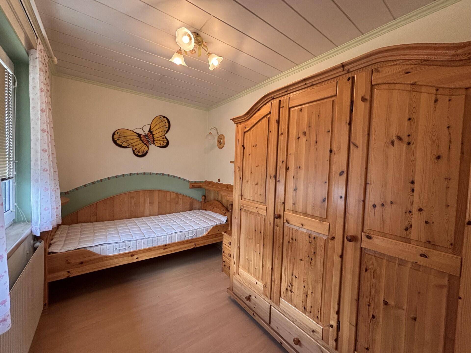 Schlafzimmer im Landhausstil mit Holzschrank, Einzelbett und Holzbalkendecke.