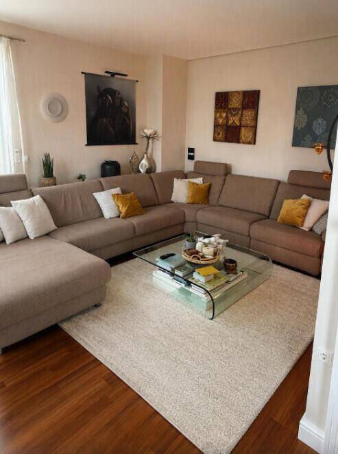 Gemütliches Wohnzimmer mit großem Ecksofa, Glastisch und hellem Teppich, ideal zum Entspannen.