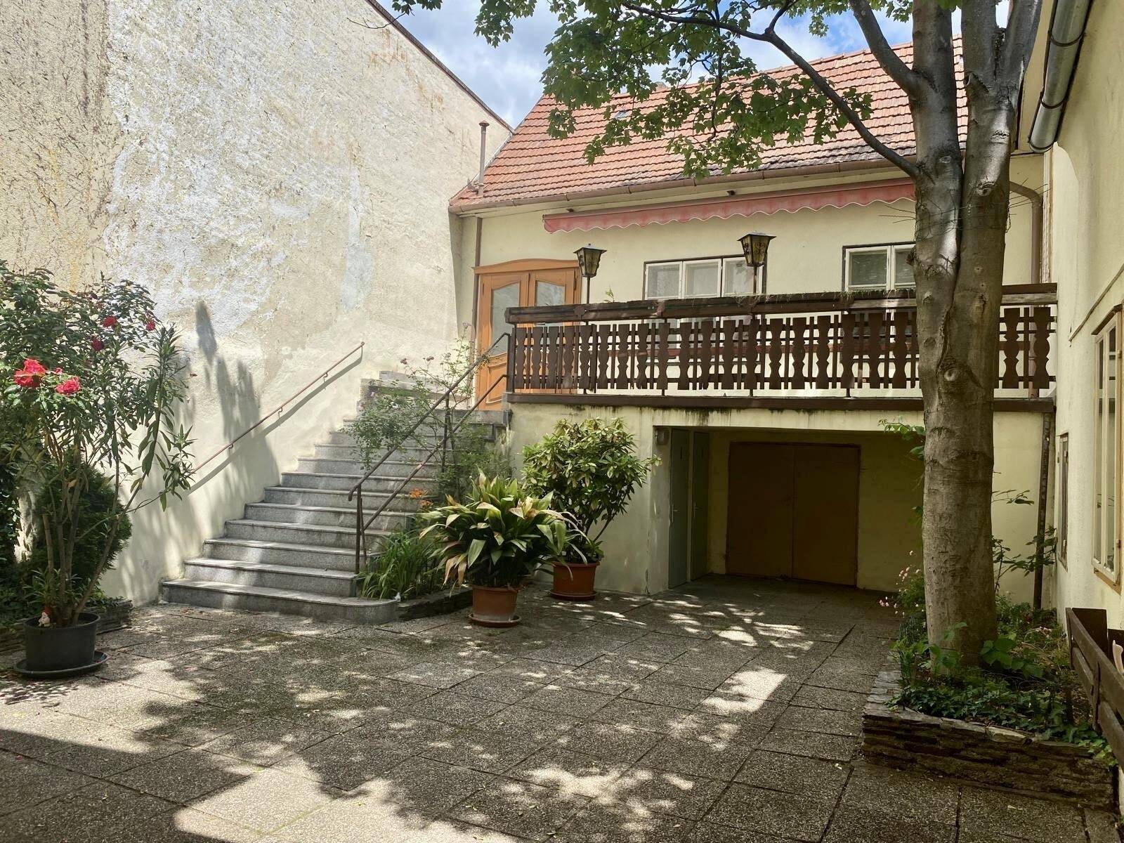 Geräumiger Hinterhof mit Außentreppe, Balkon und einem großen Baum, der Schatten spendet.
