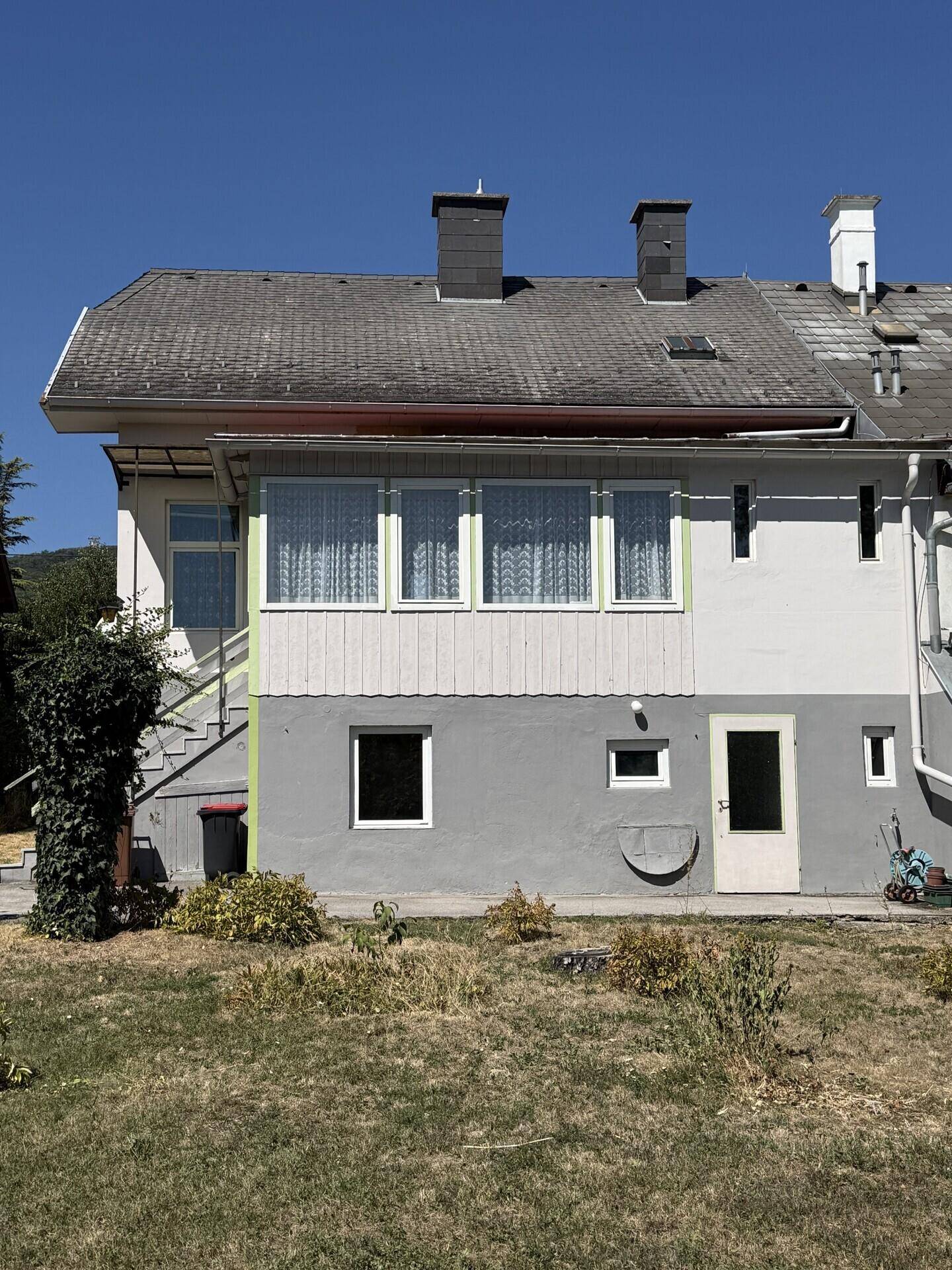 Rückansicht des Hauses mit einem großen, trockenen Garten und einer Terrasse im Erdgeschoss.