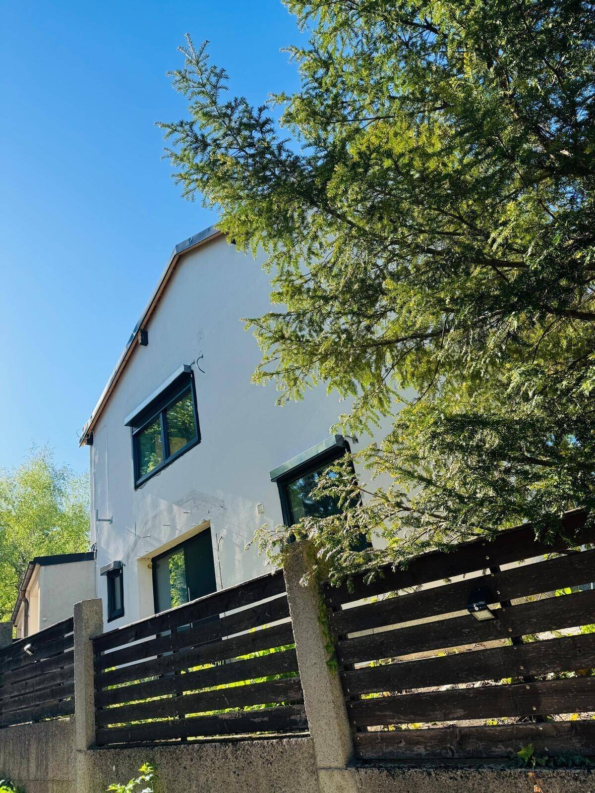 Seitenansicht des Hauses mit grüner Umgebung und einem Holzzaun im Vordergrund.