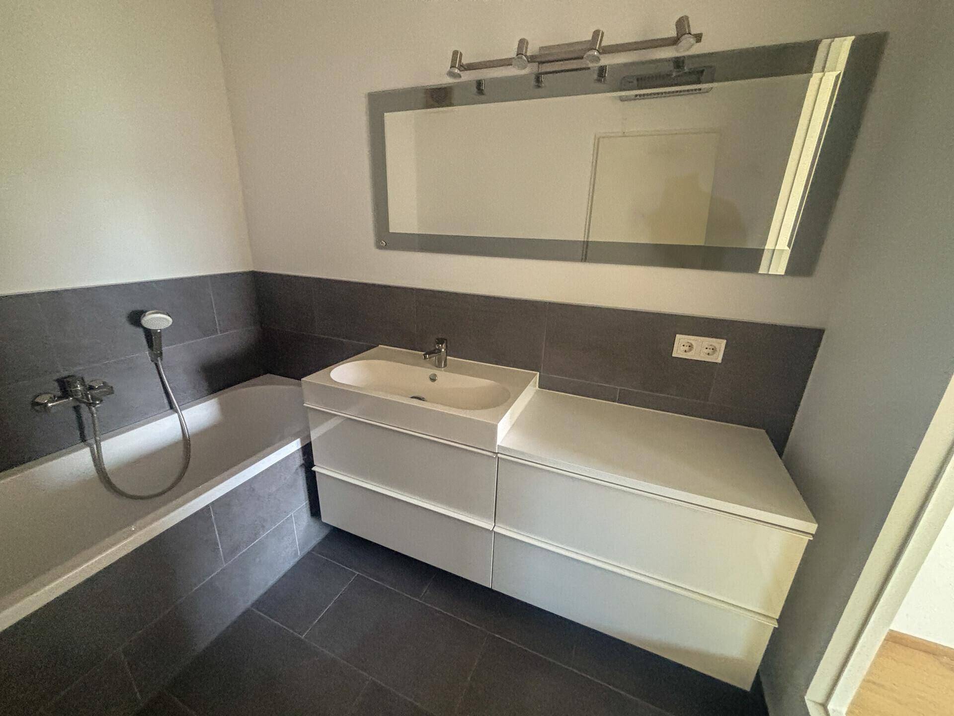 Stilvolles Badezimmer mit Badewanne, modernem Waschtisch und großem Wandspiegel.