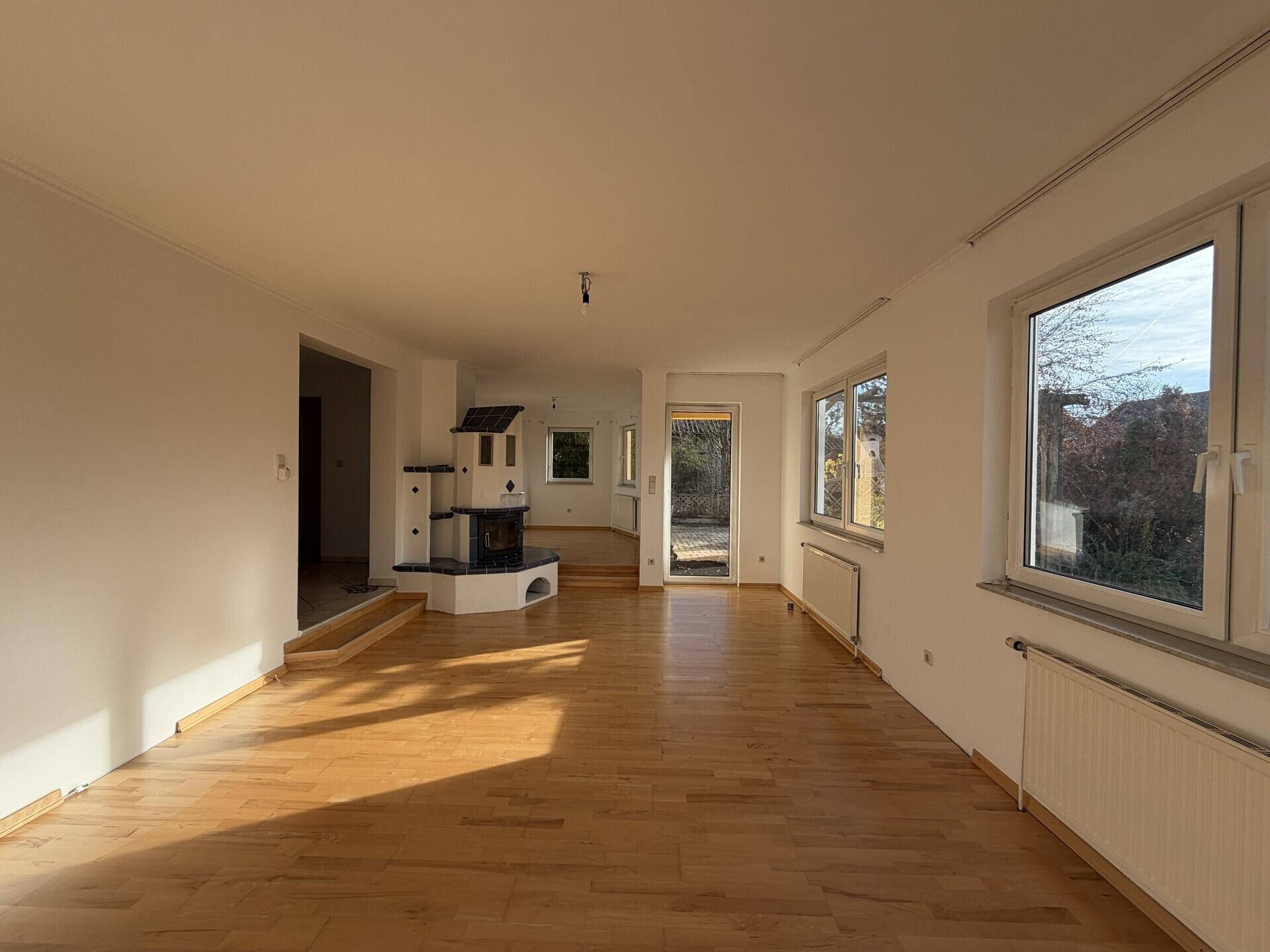 Helles Wohnzimmer mit Parkettboden, großen Fenstern und einem traditionellen Kachelofen.