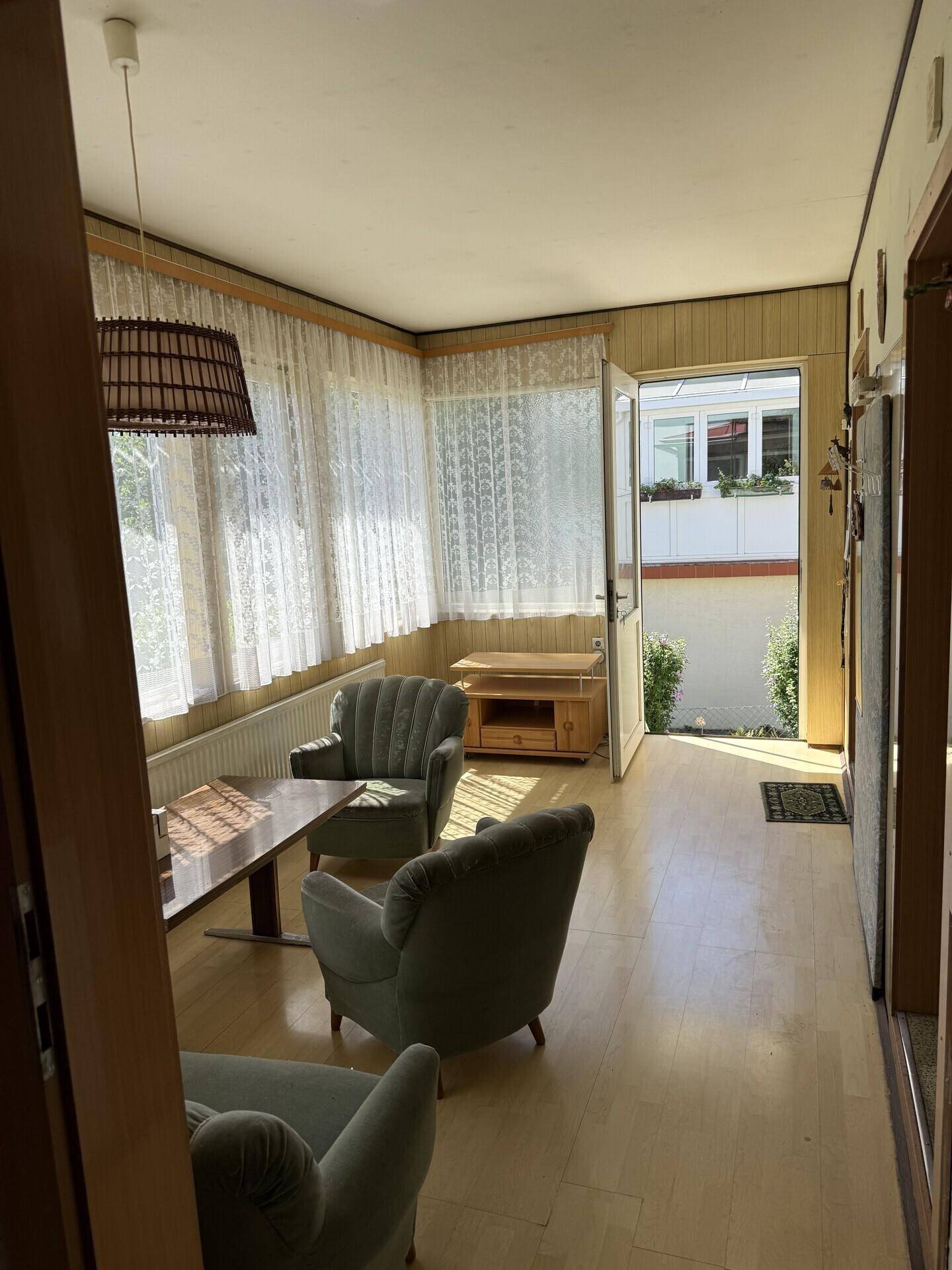Heller Wintergarten mit Vintage-Sesseln, Holzboden und vielen Fenstern, die viel Licht hereinlassen.