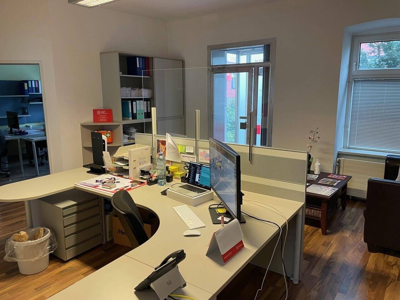 Modern eingerichtetes Büro mit Schreibtisch, Computer und Blick auf den Außenbereich durch die Tür.