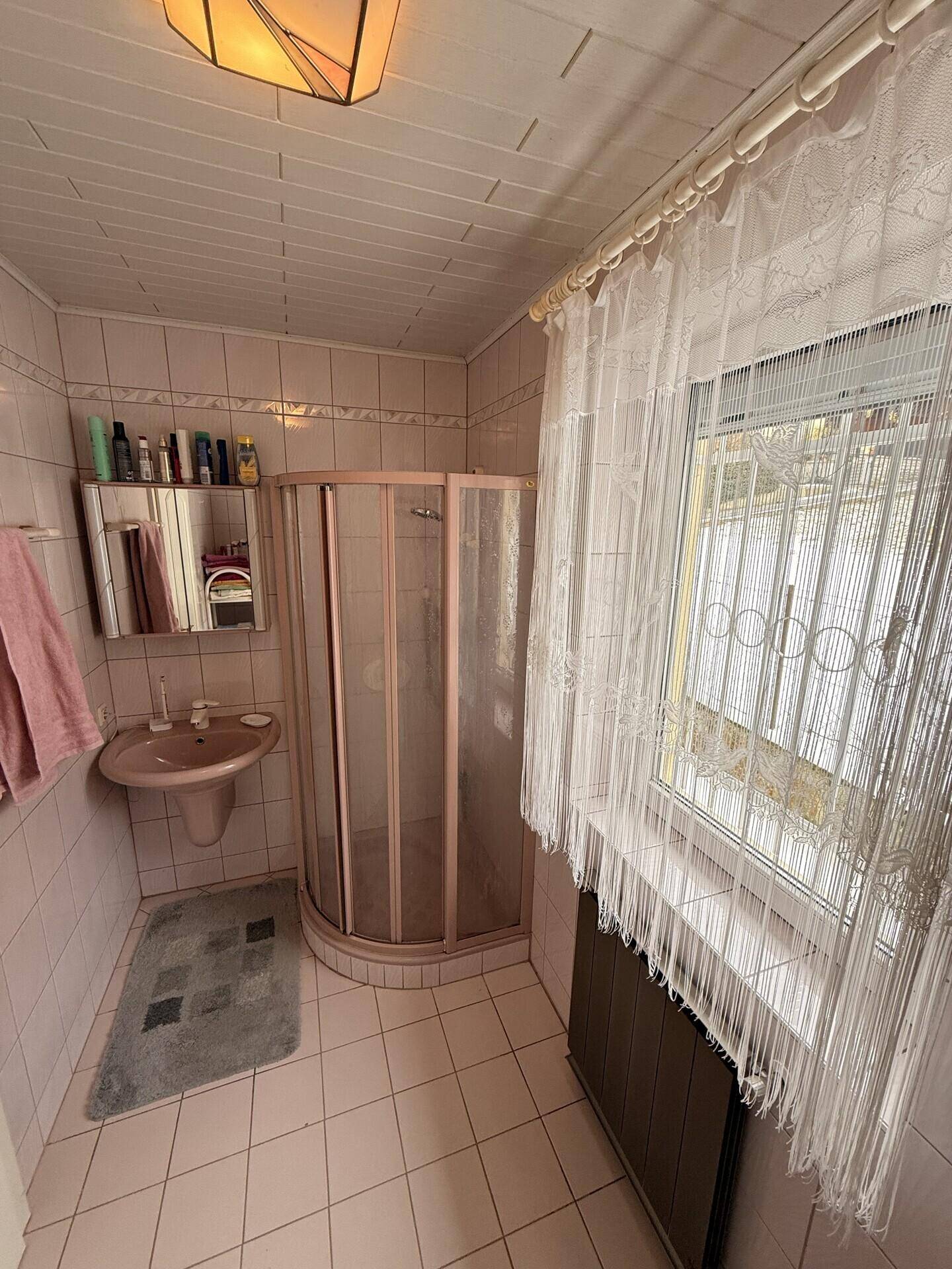 Badezimmer mit rosa Fliesen, Duschkabine und Waschbecken in originalem Zustand.
