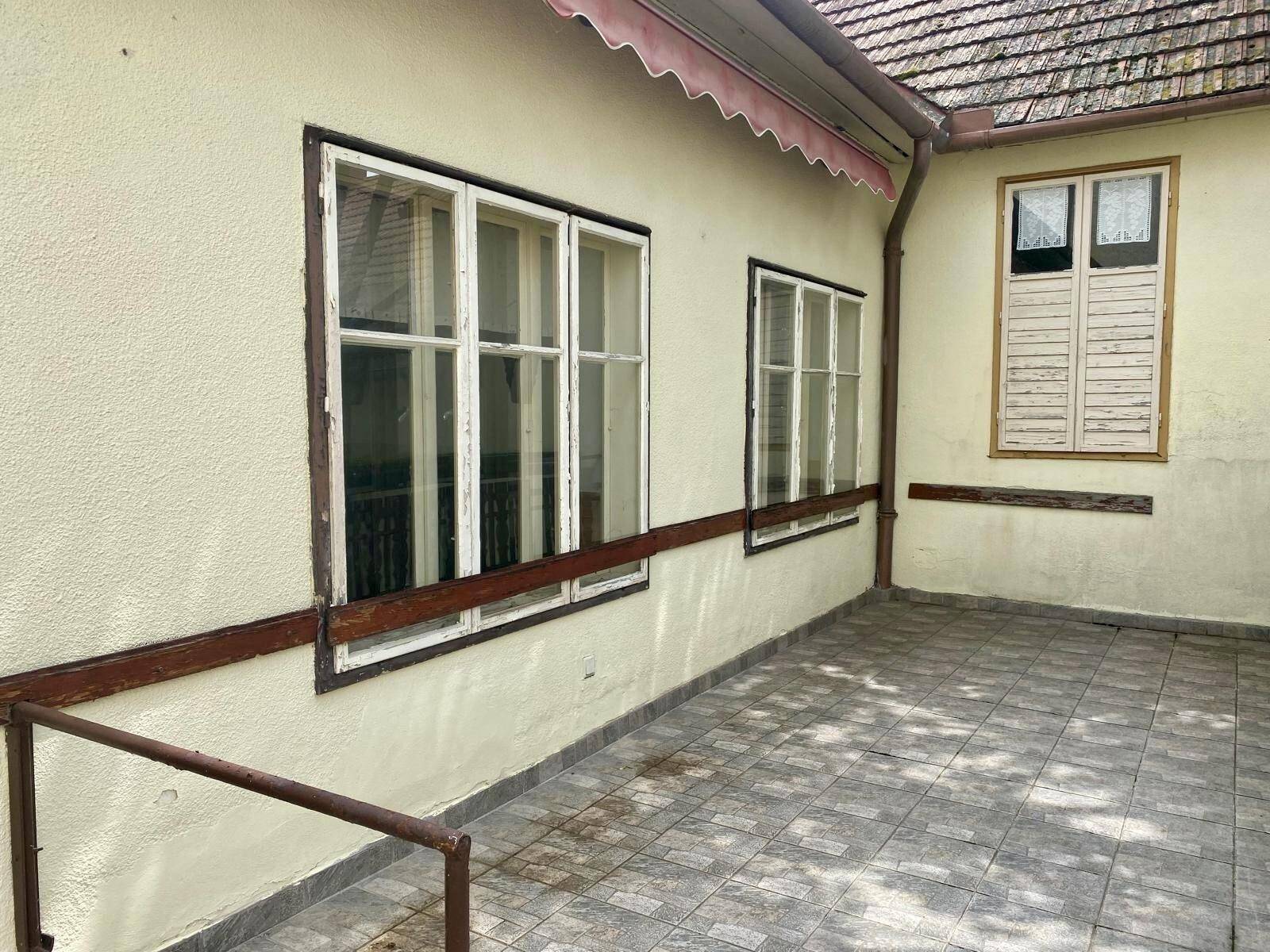 Gepflasterte Terrasse am Gebäude mit Blick auf die Fenster und eine Markise.