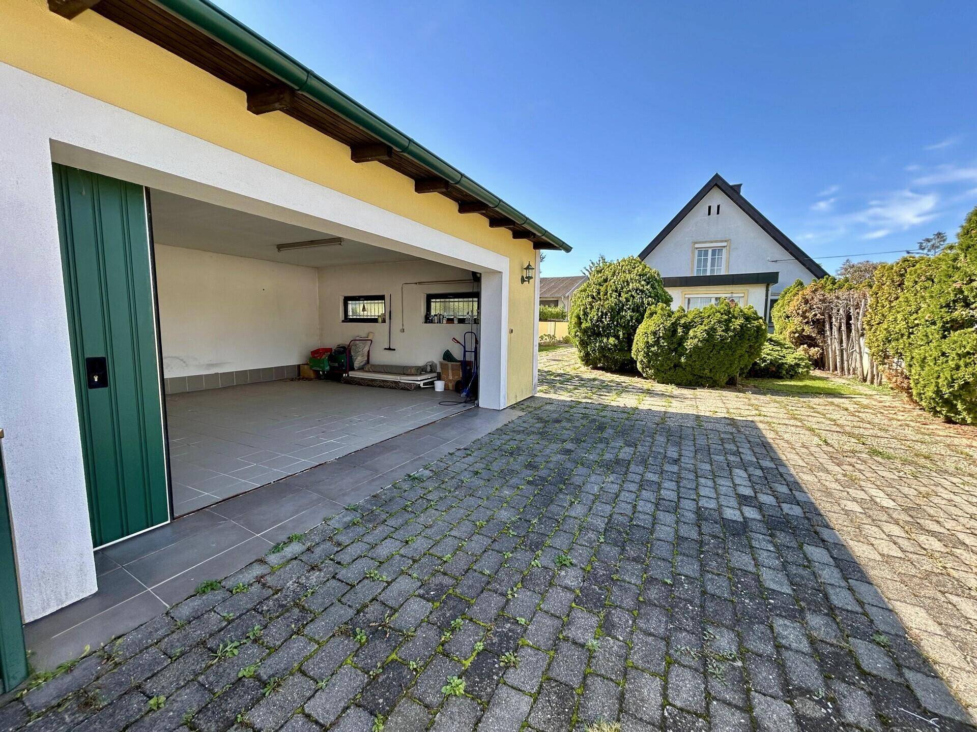 Gelbe Garage mit grünen Toren und gepflasterter Einfahrt vor einem Wohnhaus.