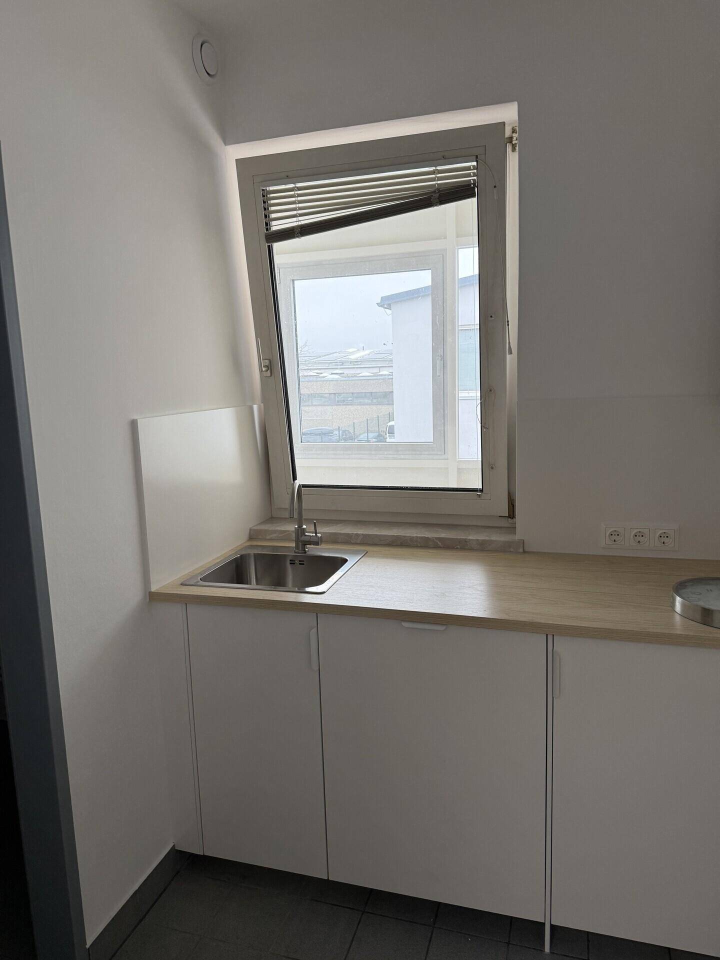 Kleine Küchenzeile mit weißen Schränken, einer Arbeitsplatte aus Holz und einer Spüle unter einem Fenster.