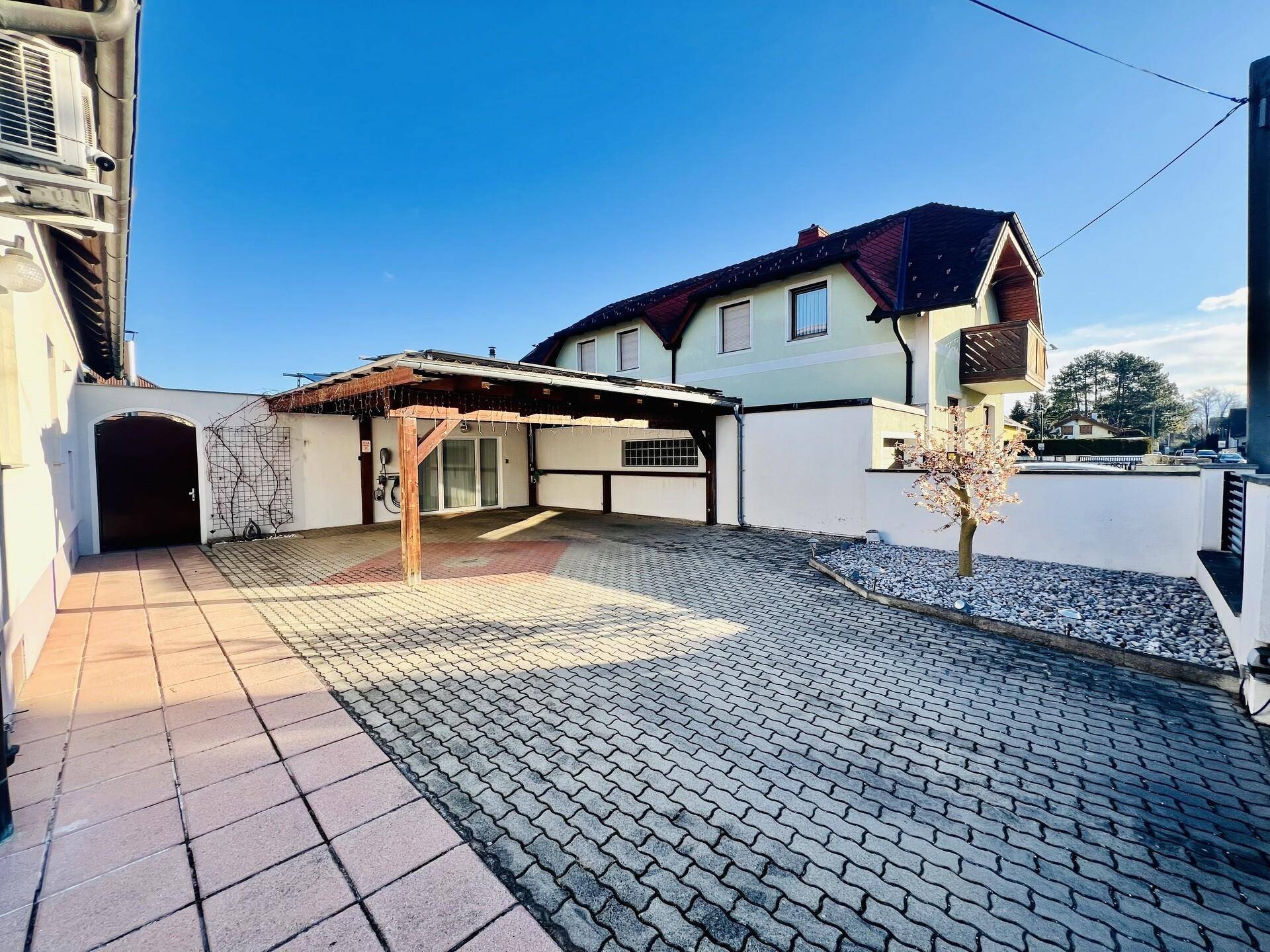Gepflasterte Einfahrt mit einem Carport und einem weiteren Gebäude im Hintergrund.