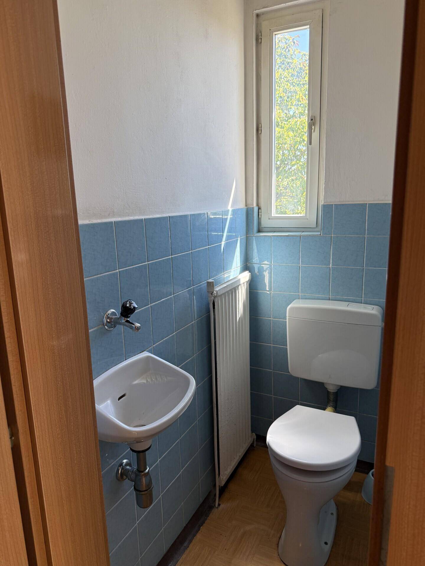 Kleines Gäste-WC mit blauen Fliesen, Fenster und einem einzelnen Waschbecken.