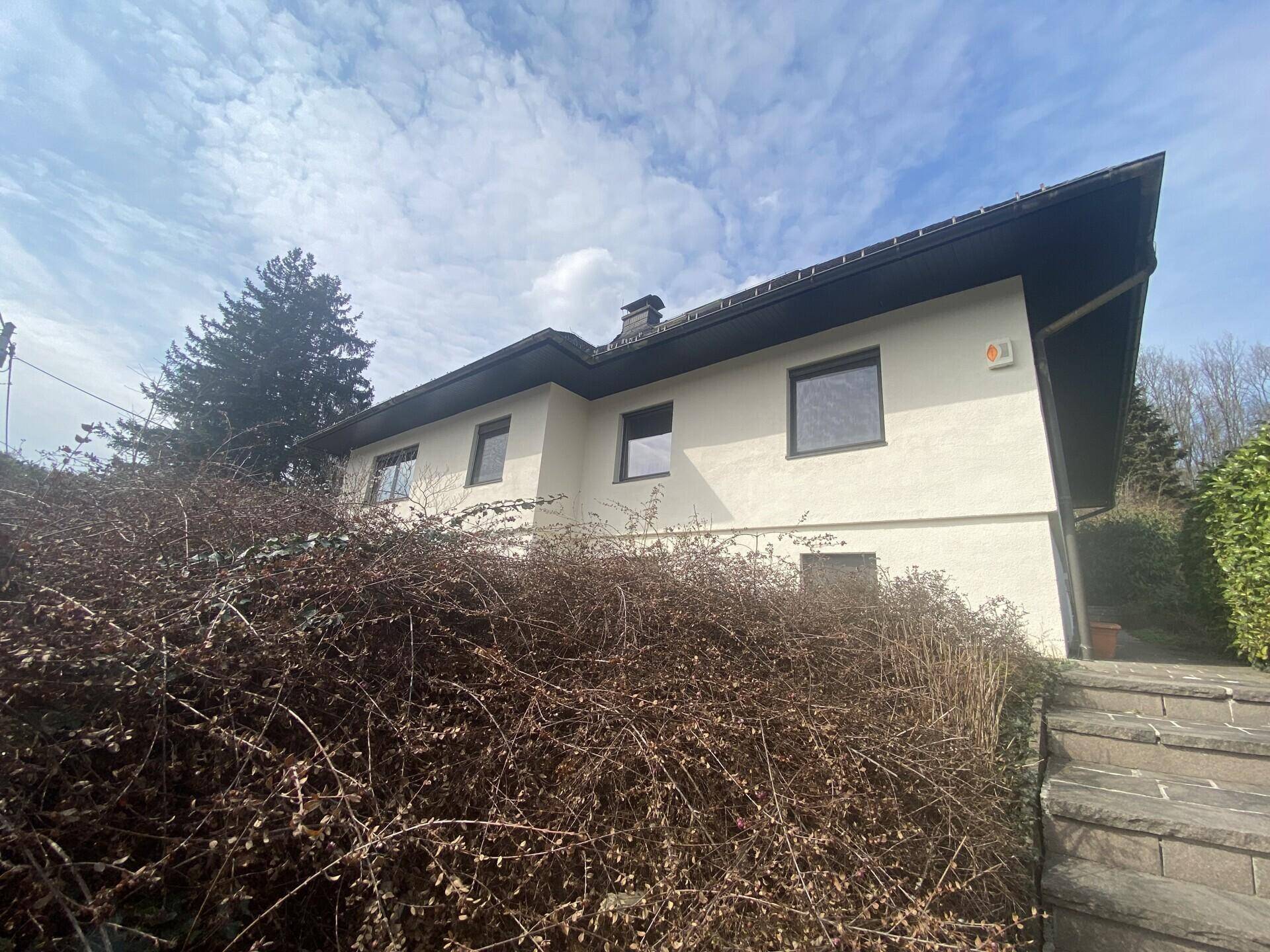Seitenansicht des Hauses mit weißer Fassade, dunklen Fenstern und einer Treppe zum Garten.