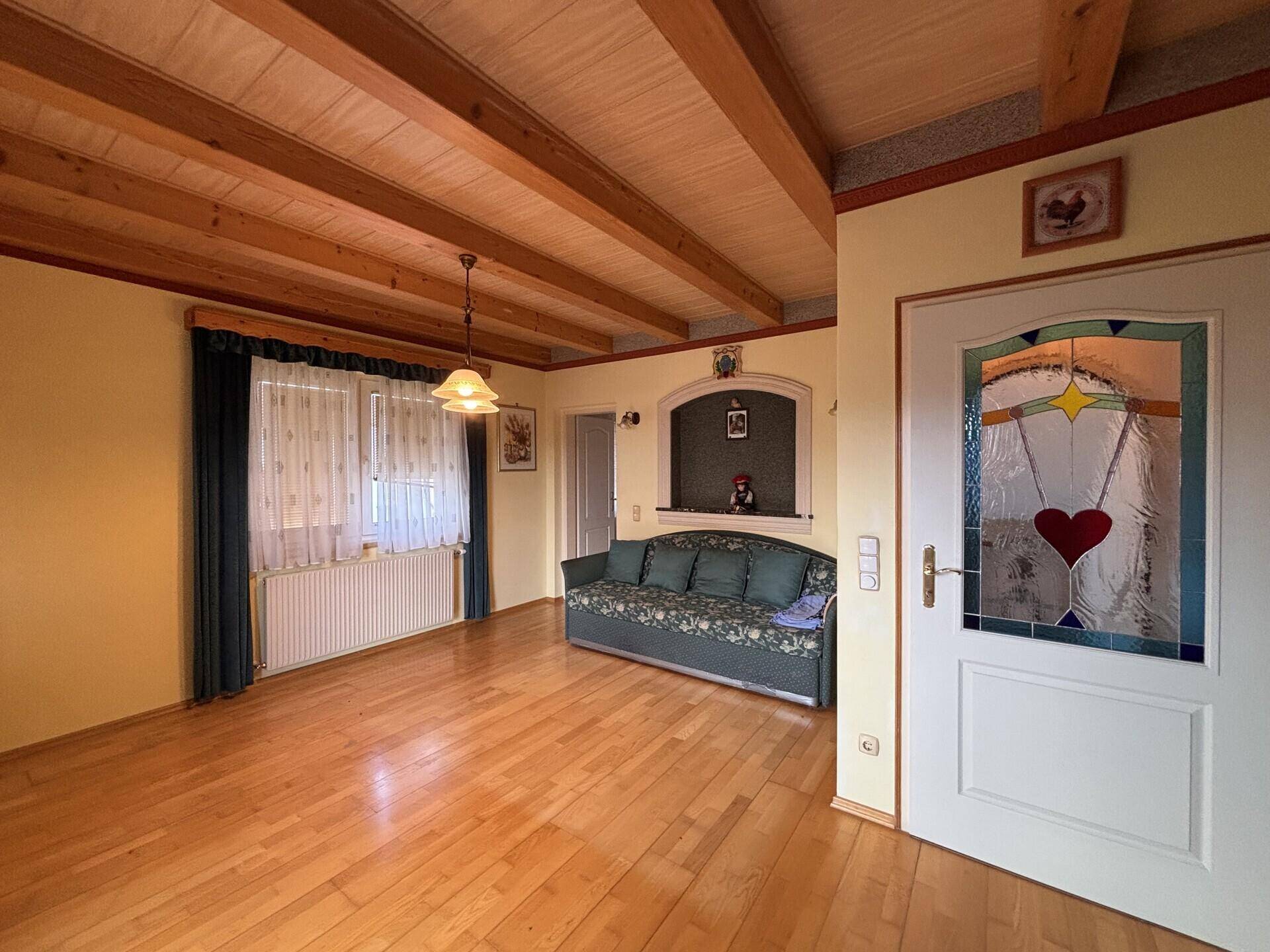 Helles Wohnzimmer mit Holzbalkendecke, Parkettboden und einer gemütlichen Couch.