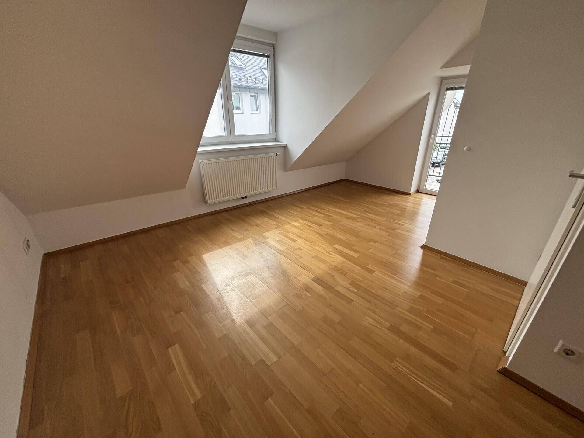 Dachgeschosszimmer mit Parkettboden, schrägen Wänden und Zugang zu einem Außenbereich.