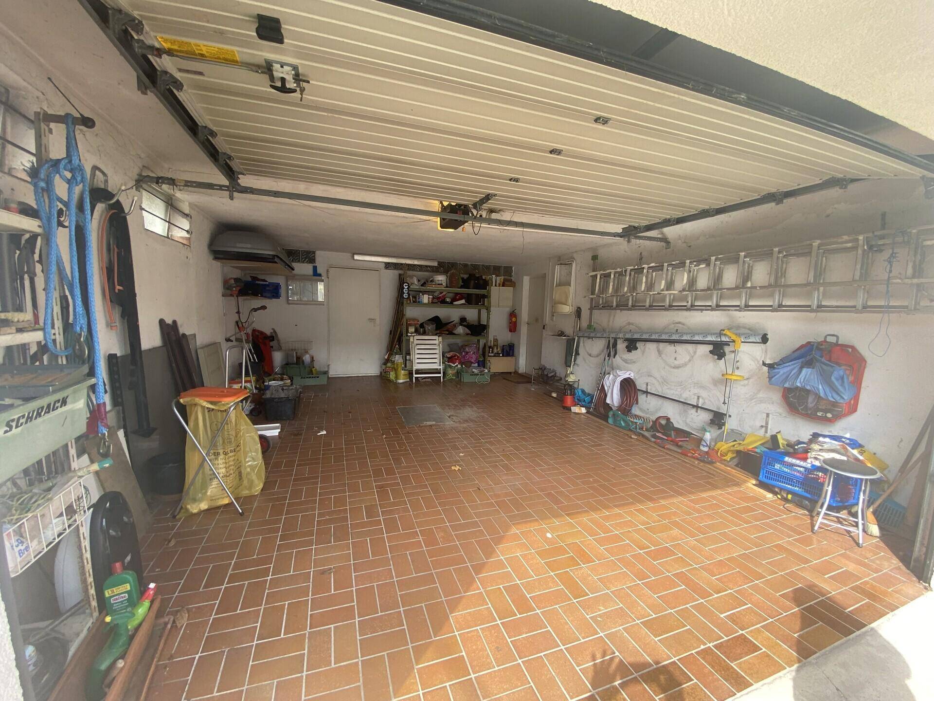 Geräumige Garage mit Fliesenboden, Stauraum und einem geöffneten Garagentor.