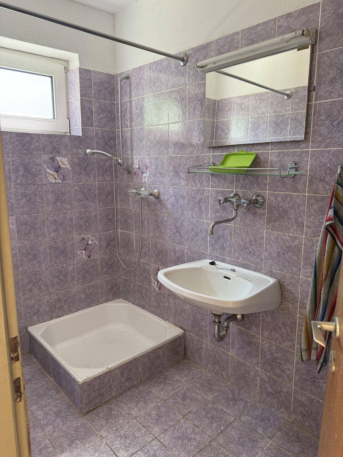 Badezimmer mit lila Fliesen, Waschbecken und einer Duschwanne, die zum Duschen einlädt.