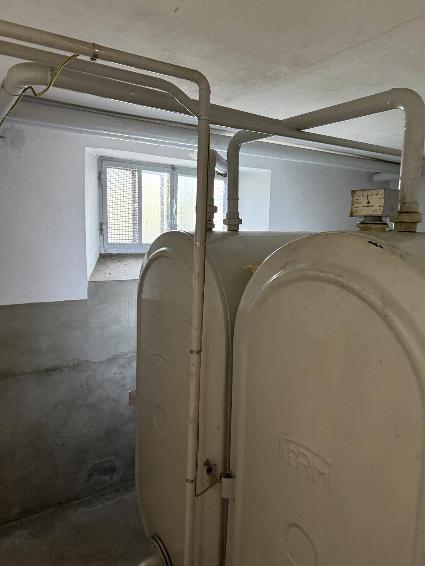 Kellerraum mit großen Öltanks und einem Fenster, dient als Lager- und Technikbereich.
