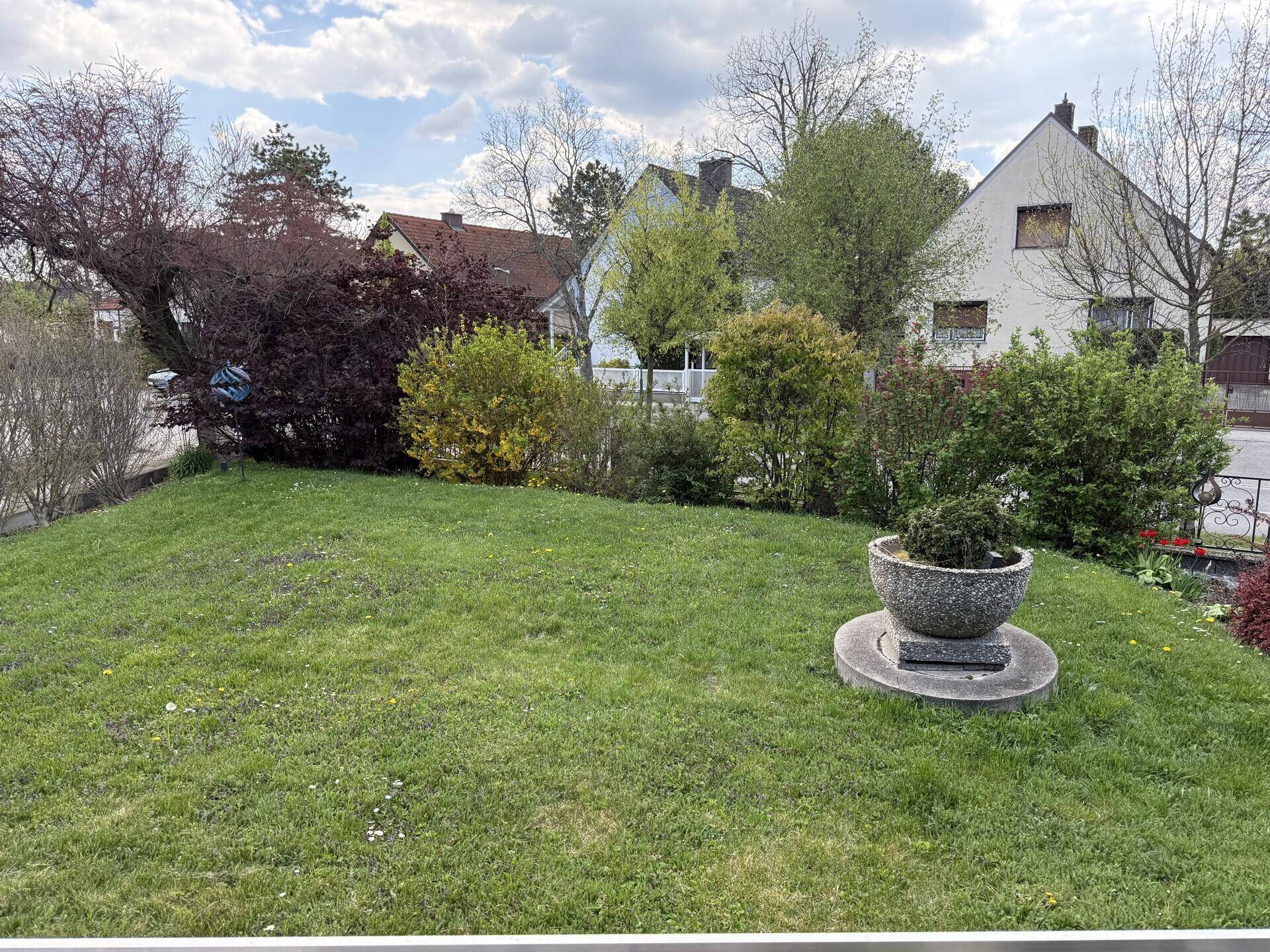 Weitläufiger Rasenbereich mit Blumenkübel und Blick auf die Nachbarschaft.