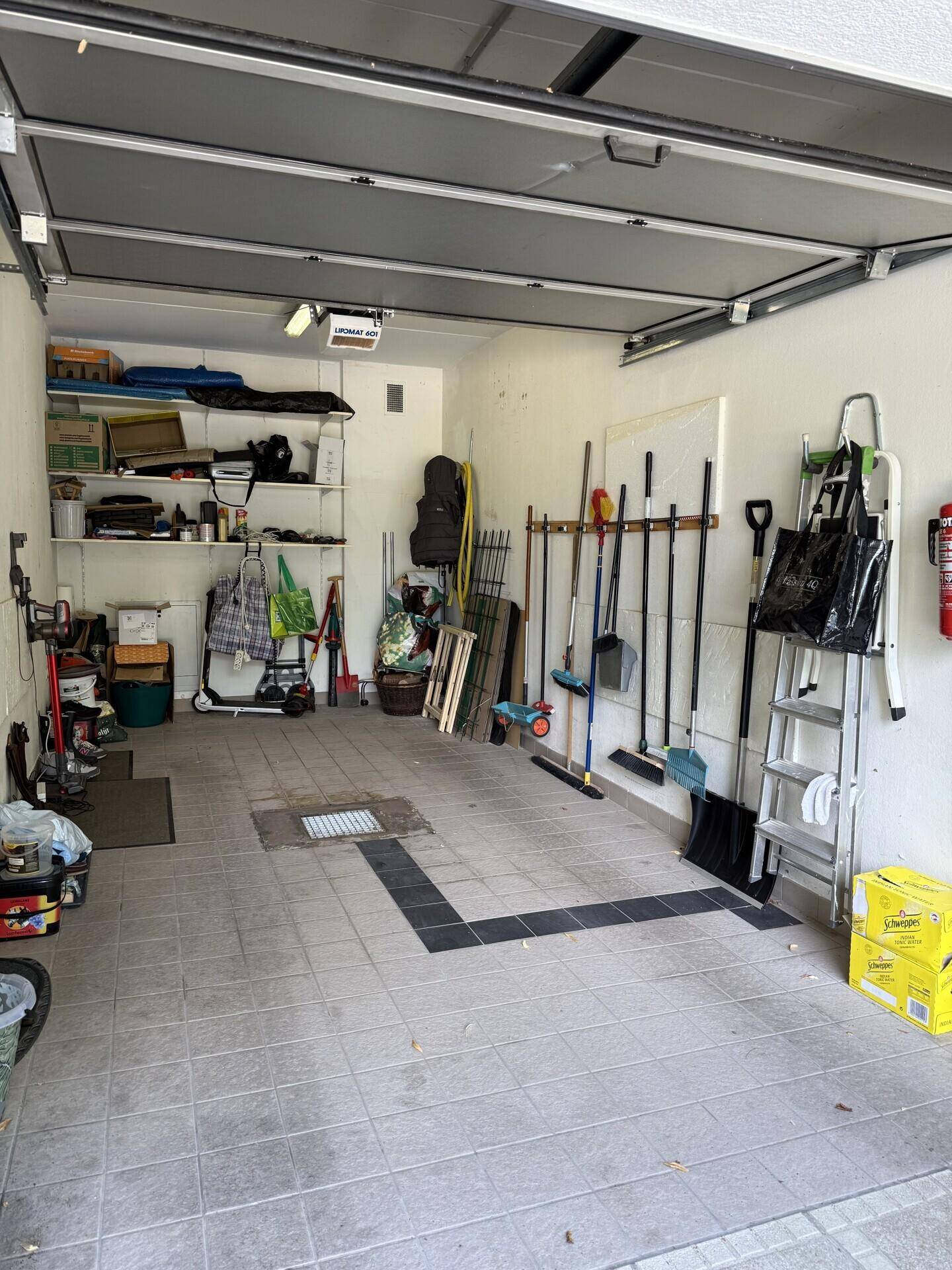 Geräumige Garage mit Fliesenboden, Stauraum und Werkzeugen an der Wand.