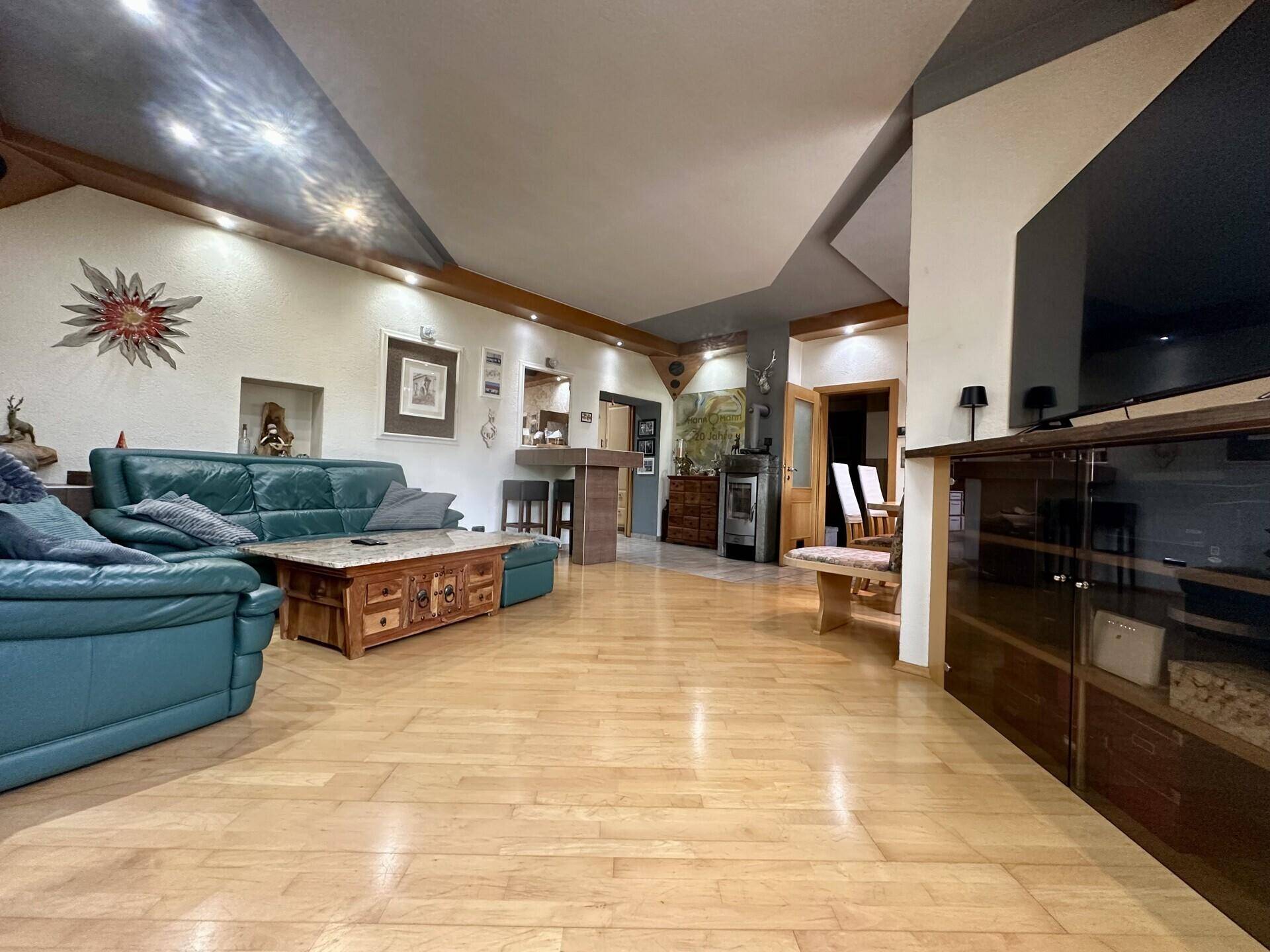 Großzügiges Wohnzimmer mit hellem Holzfußboden, Ledersofas und einer kleinen Bar im Hintergrund.