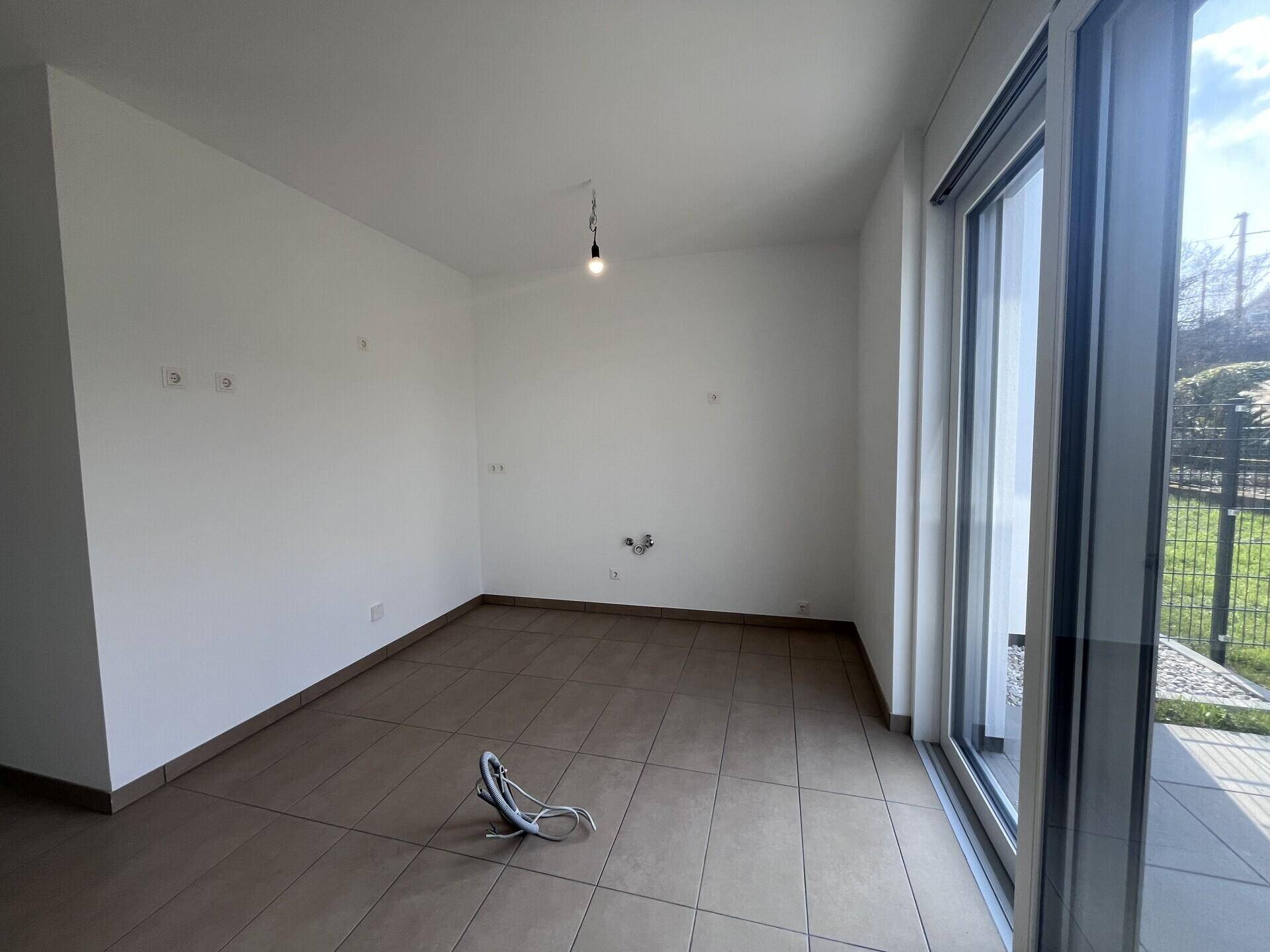 Heller Raum mit Fliesenboden und Zugang zur Terrasse, vorbereitet für eine Küche.
