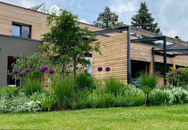 Detailansicht des gepflegten Gartens mit blühenden Pflanzen und moderner Holzfassade des Hauses.