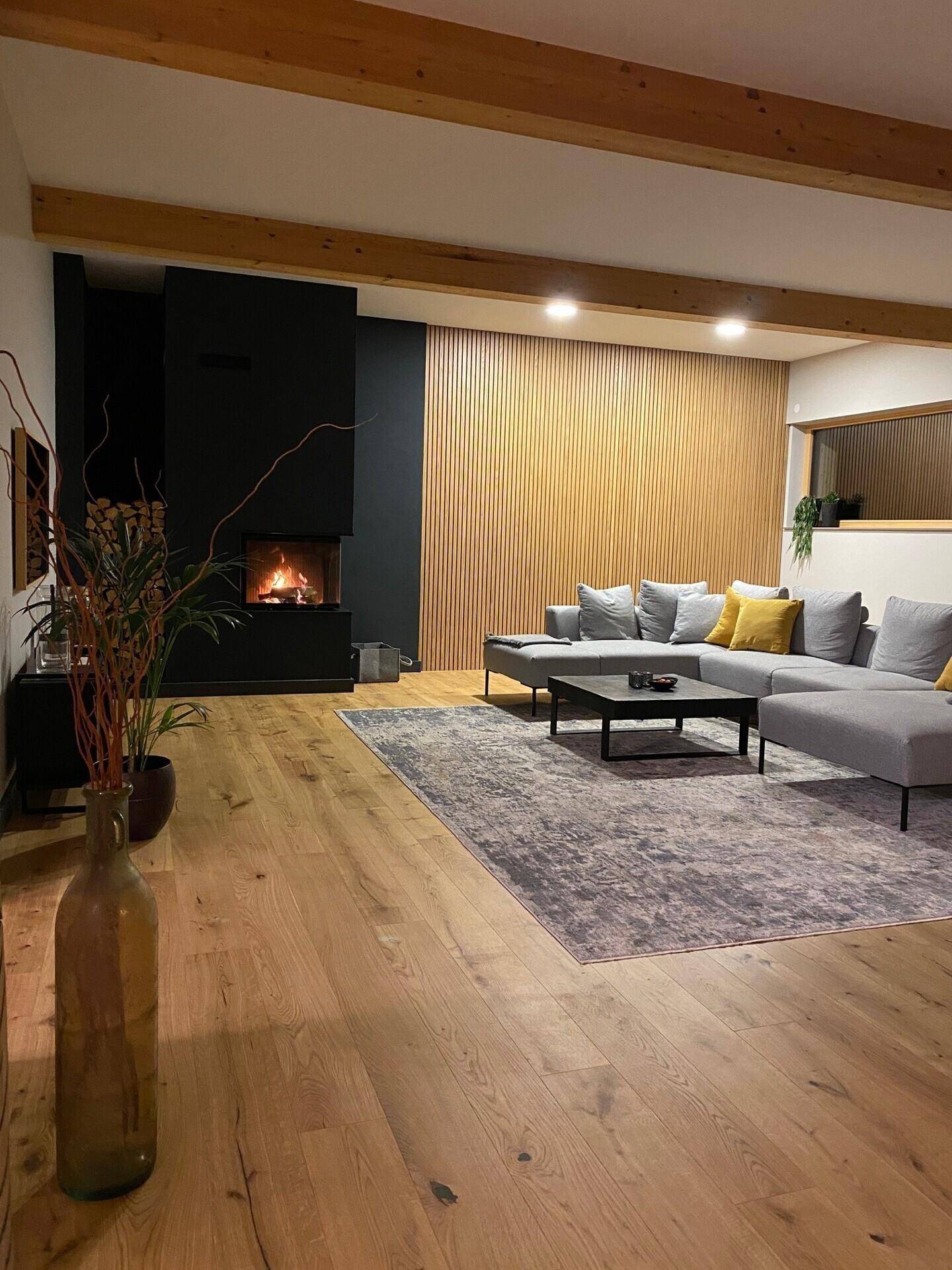 Gemütliches Wohnzimmer mit modernem Kamin, Holzbalken und einer Akzentwand aus Holzlamellen.
