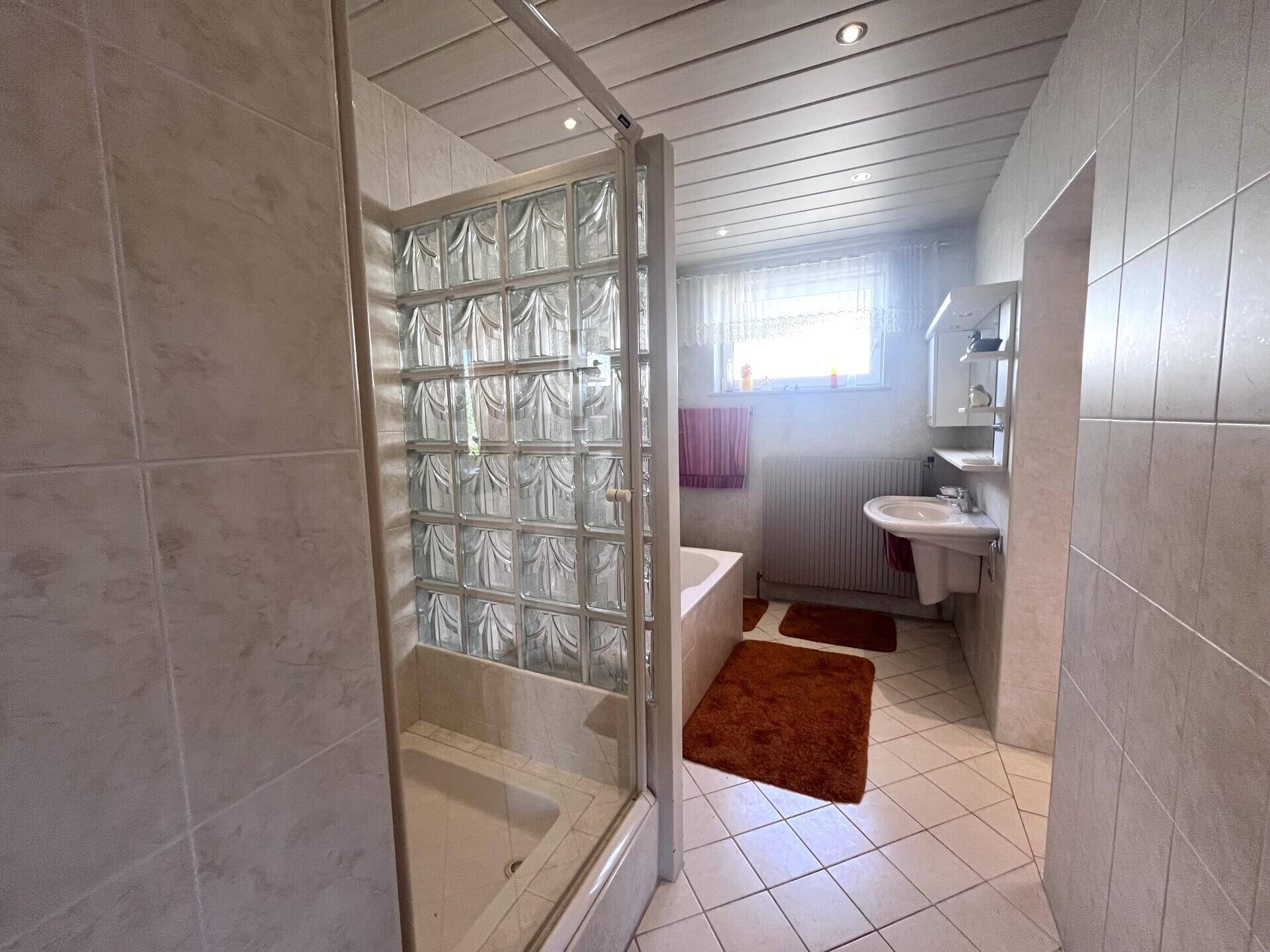 Helles Badezimmer mit Waschbecken, Spiegel, Fenster und Dusch-Badewannen-Kombination.