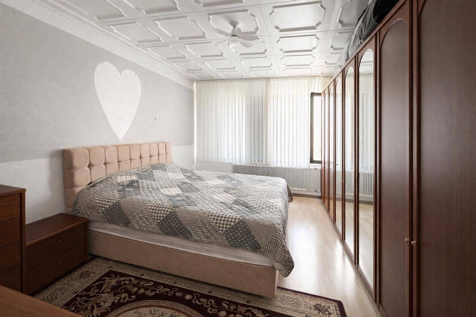 Helles Schlafzimmer mit Doppelbett, Spiegelschrank und dekorativer Kassettendecke.