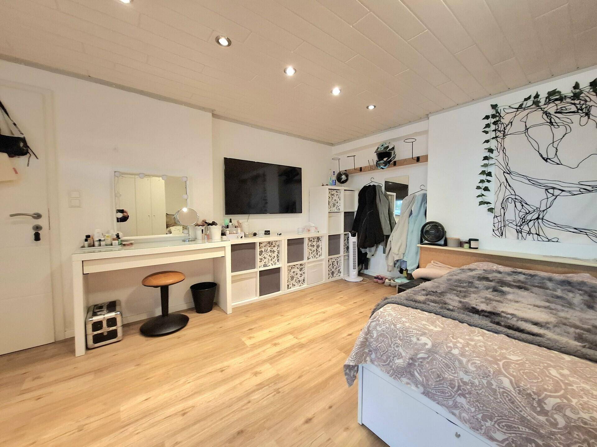 Modernes Schlafzimmer mit Schminktisch, Fernseher und Holzbalkendecke, hell und geräumig.