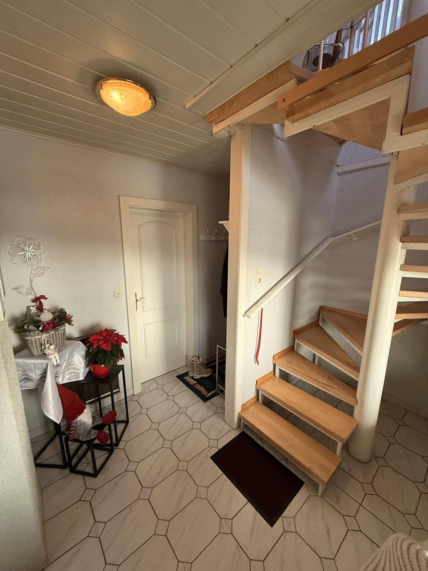Flur mit Holztreppe und gemustertem Fliesenboden in originalem Zustand.