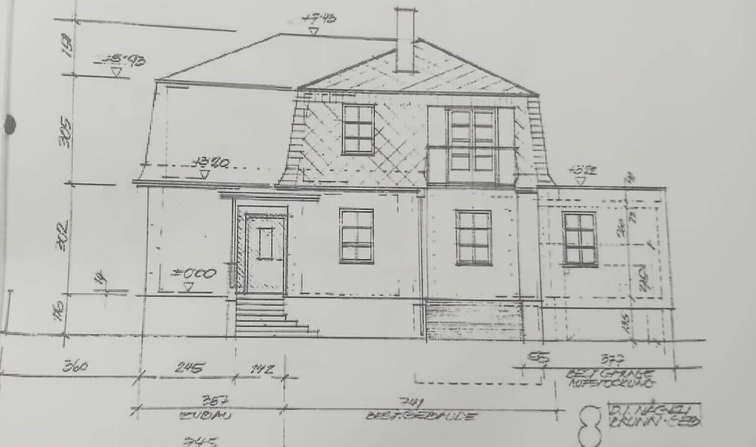 Architektonische Zeichnung der Hausfassade mit Mansarddach und detaillierten Maßangaben.
