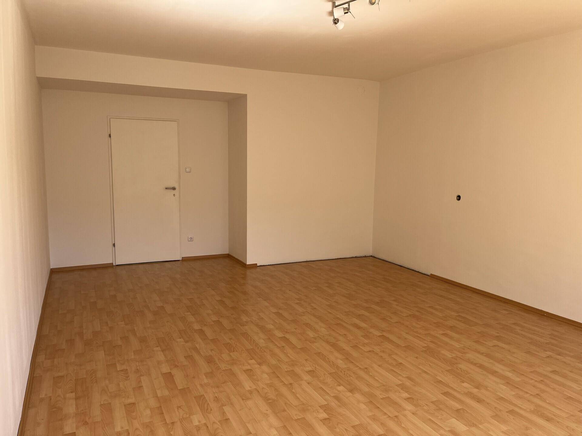 Geräumiger, leerer Raum mit hellem Laminatboden und einer Tür, bereit zur individuellen Gestaltung.