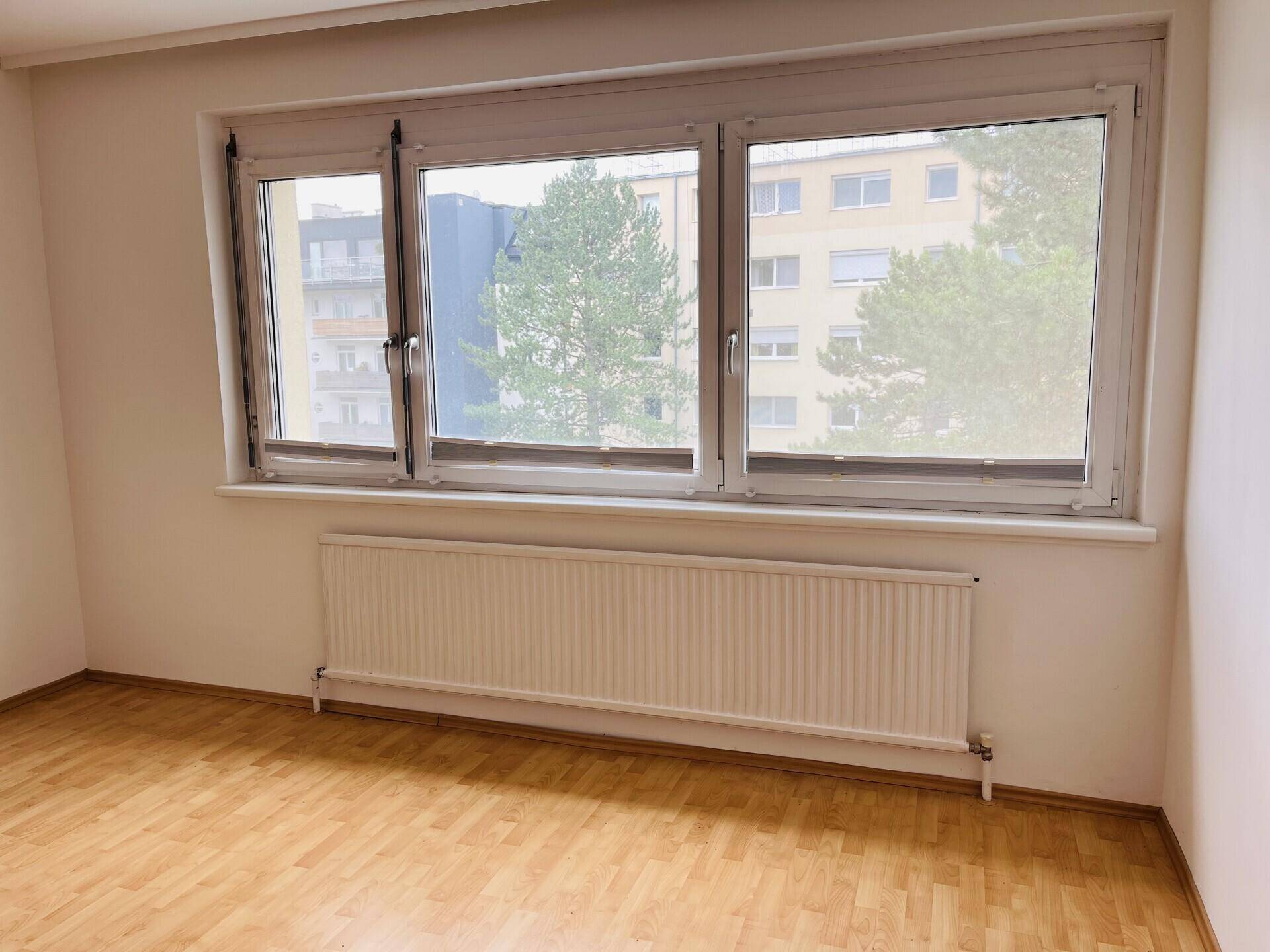 Fensterfront im Wohnzimmer mit Heizkörper und Blick auf umliegende Gebäude.