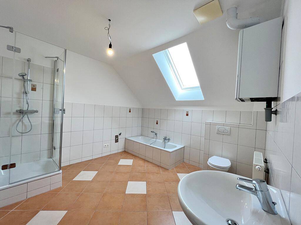 Geräumiges Badezimmer mit Dusche, Badewanne, WC, Waschbecken und einem Dachfenster für natürliches Licht.