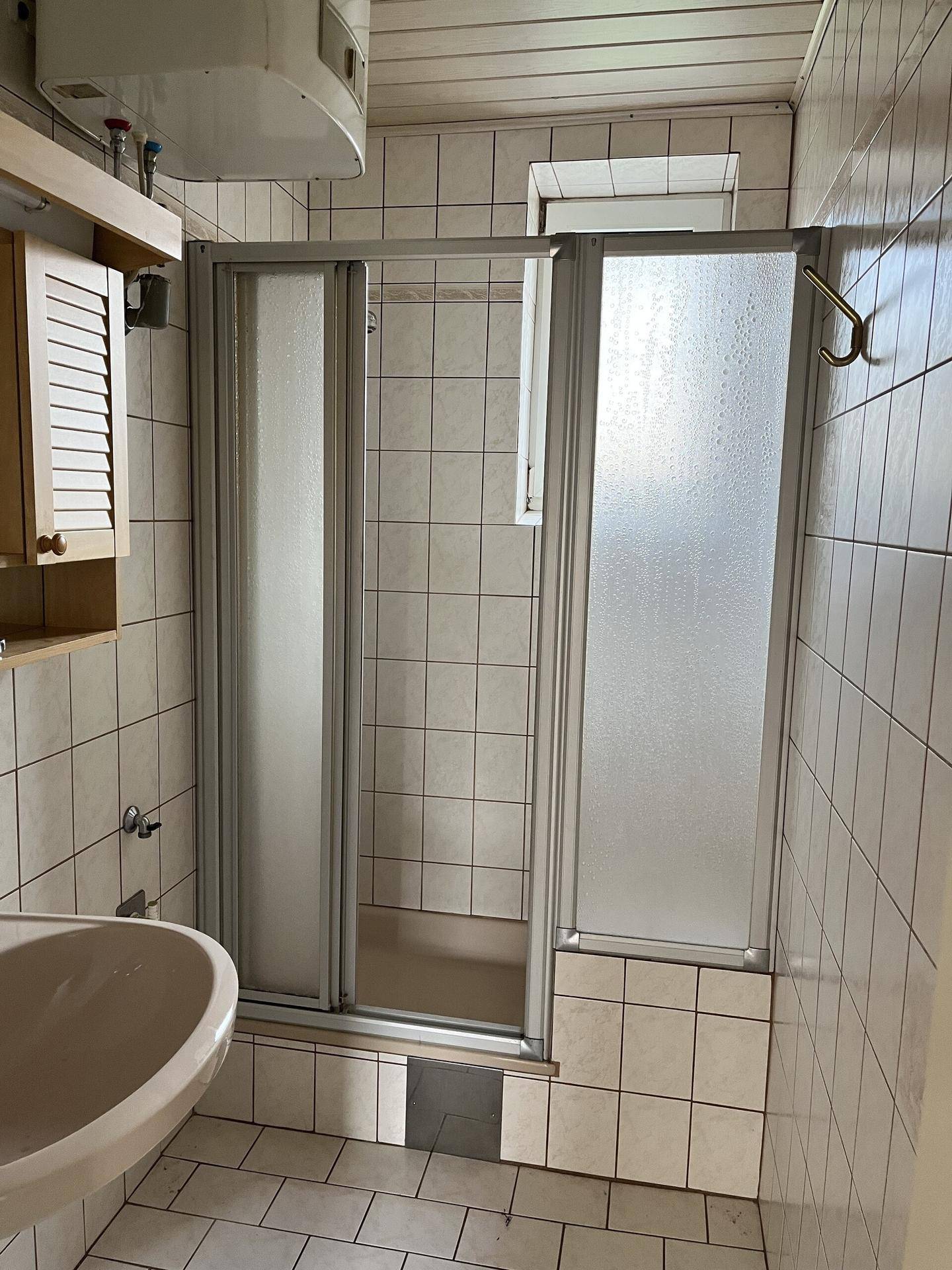 Badezimmer mit Duschkabine, Waschbecken und Fliesen an Wänden und Boden.