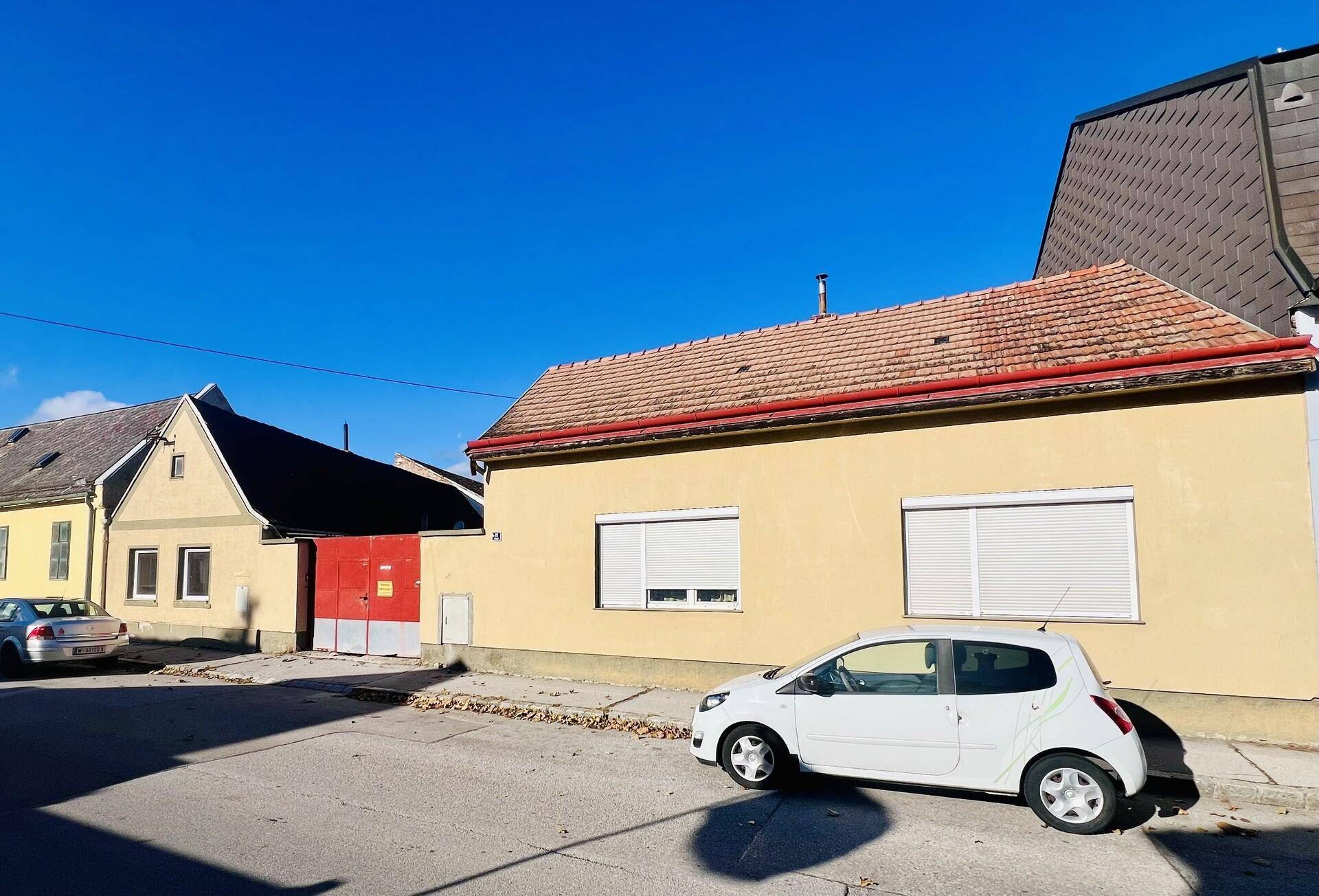 Ansicht eines gelben Hauses mit rotem Ziegeldach und Rollläden an einem sonnigen Tag.