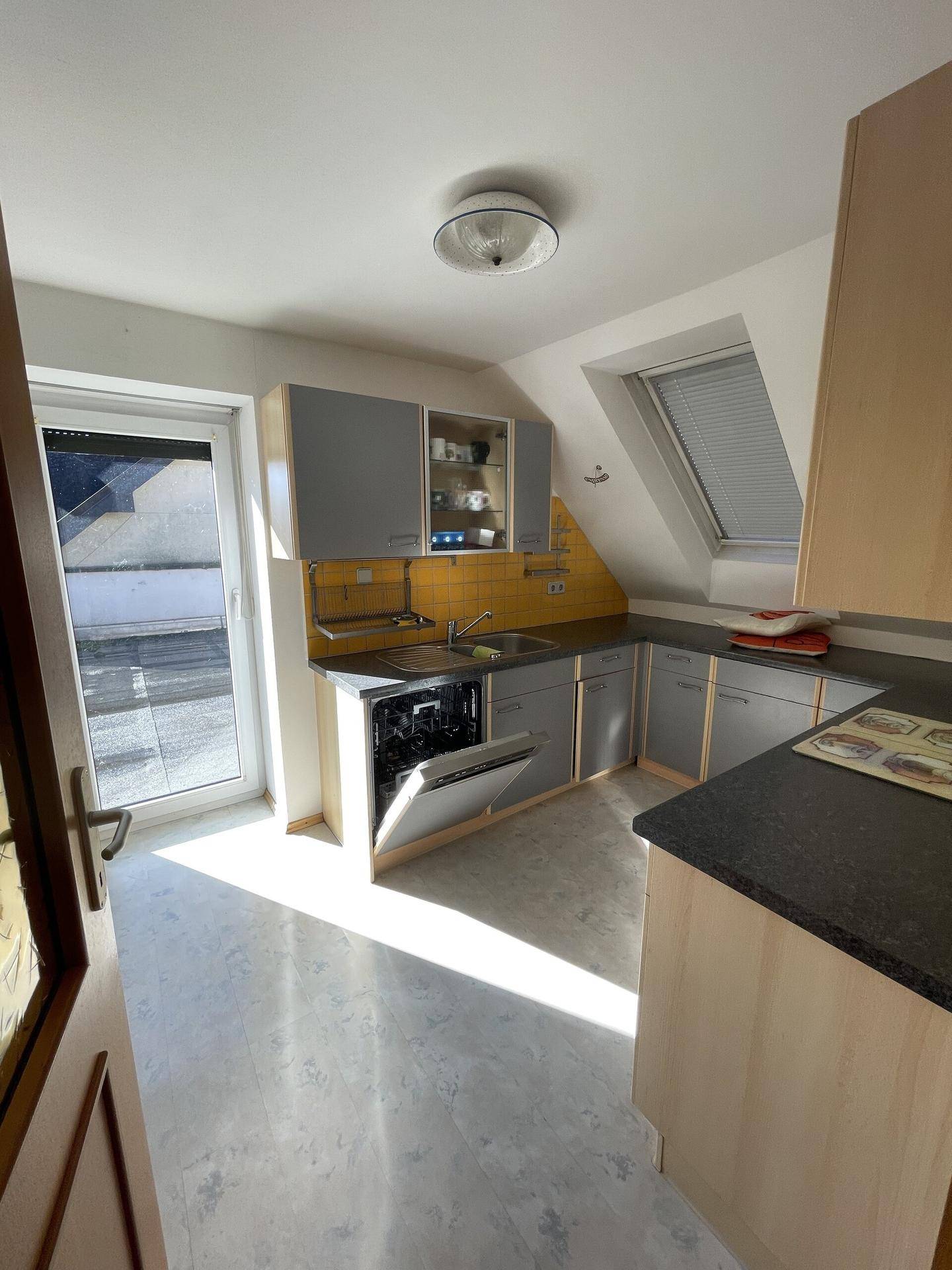 Dachgeschossküche mit grauen Schränken, Dachfenster und Zugang zur Terrasse.