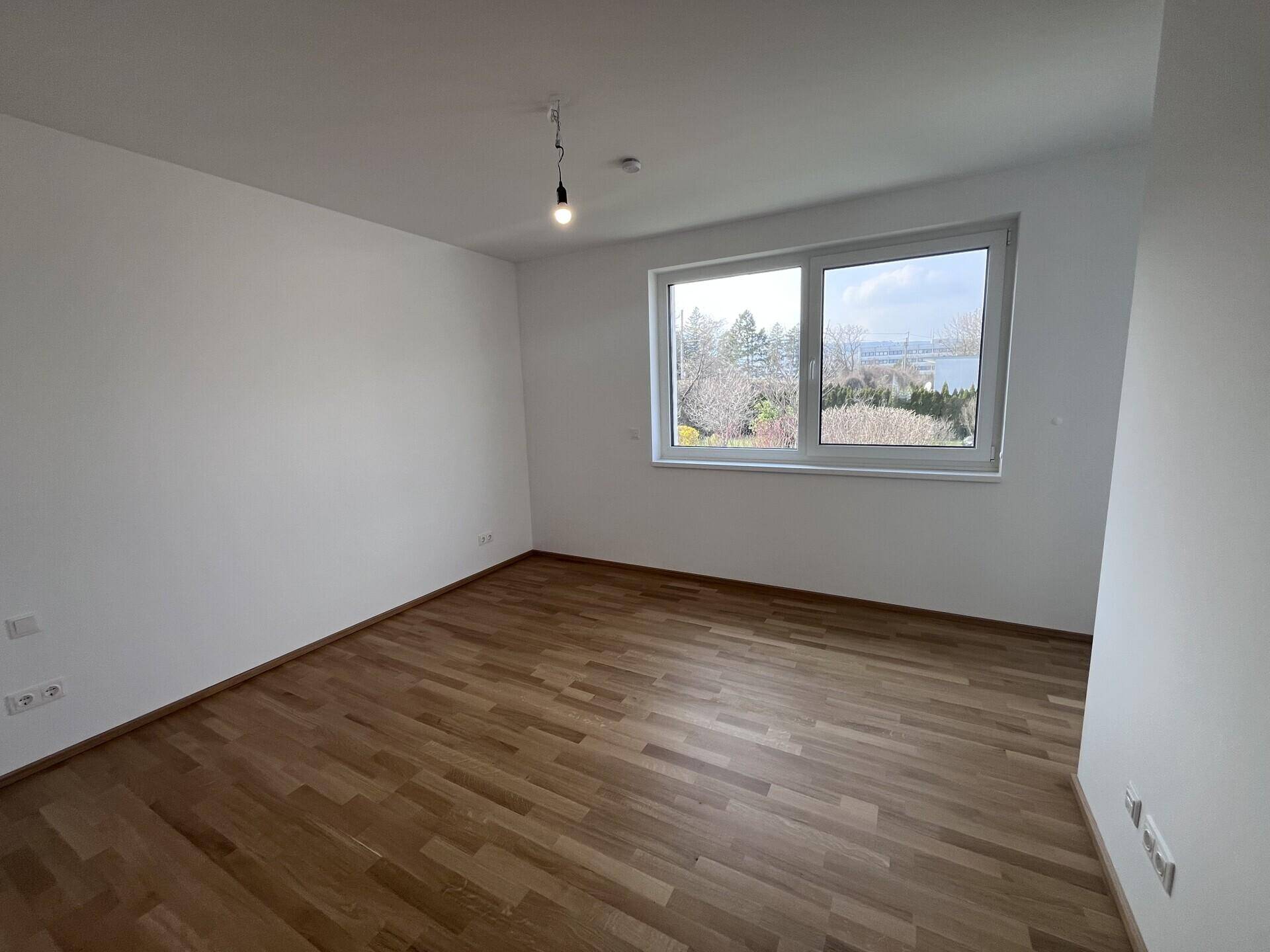 Helles Schlafzimmer mit Parkettboden und Fenster mit Blick ins Grüne.