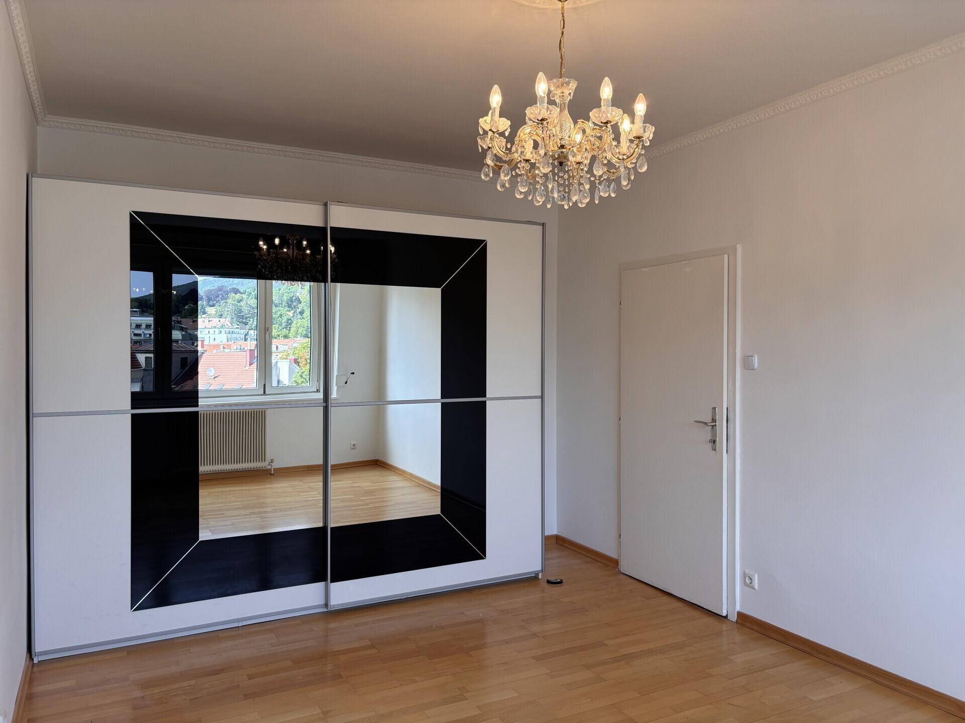 Schlafzimmer mit Spiegelschrank, Holzboden und Kronleuchter, bietet Blick auf die Stadt.