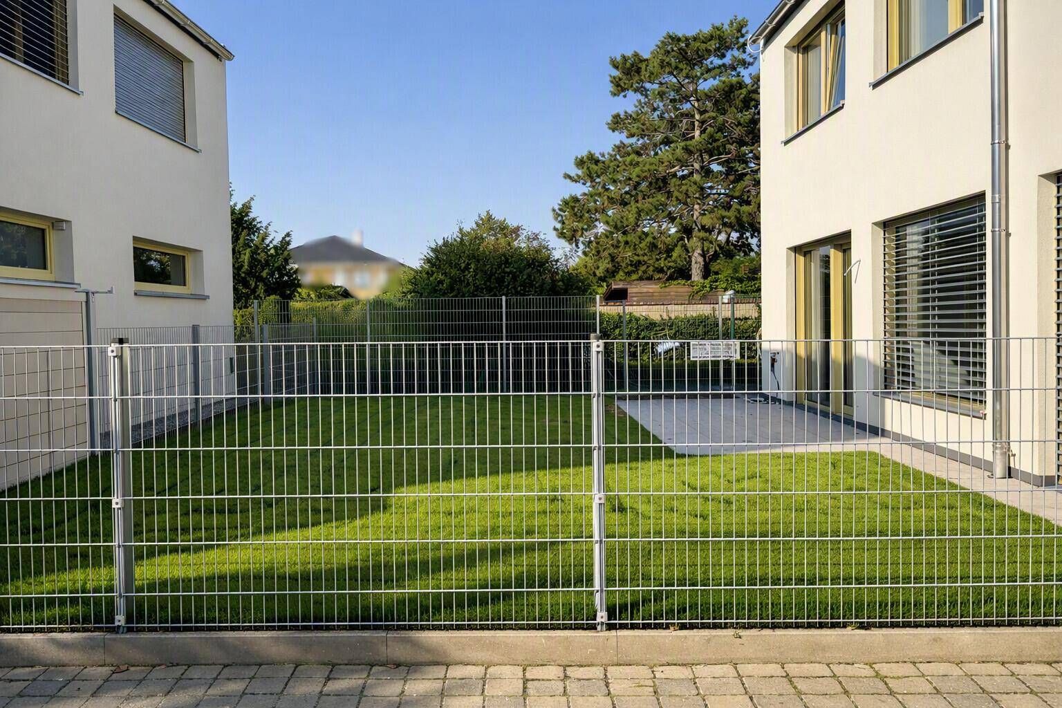 Gepflegter Gartenbereich zwischen zwei modernen Häusern mit Metallzaun und Rasenfläche.