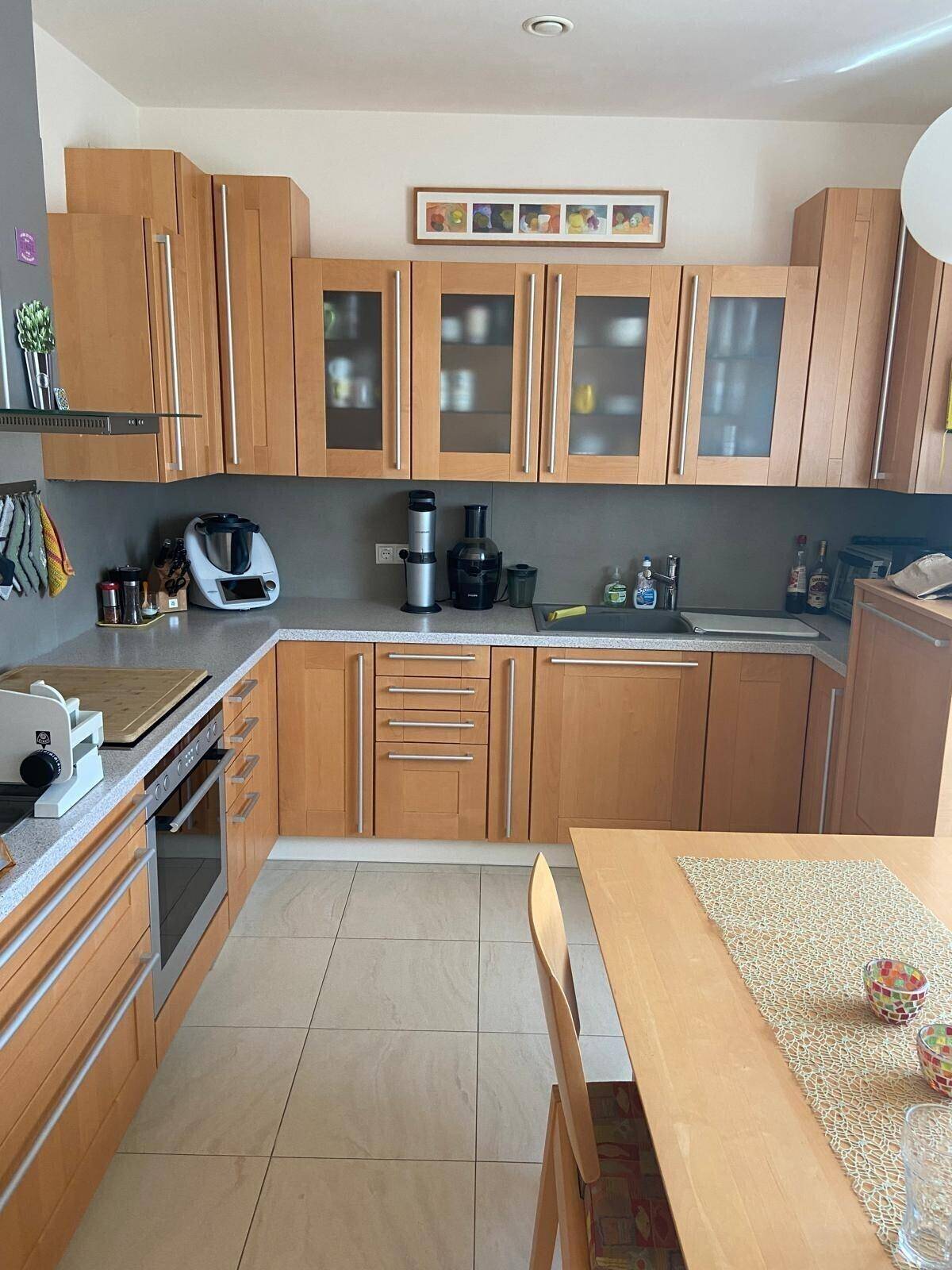 Funktionale Küche mit hellen Holzschränken, grauen Arbeitsplatten und Fliesenboden, ideal für Familien.