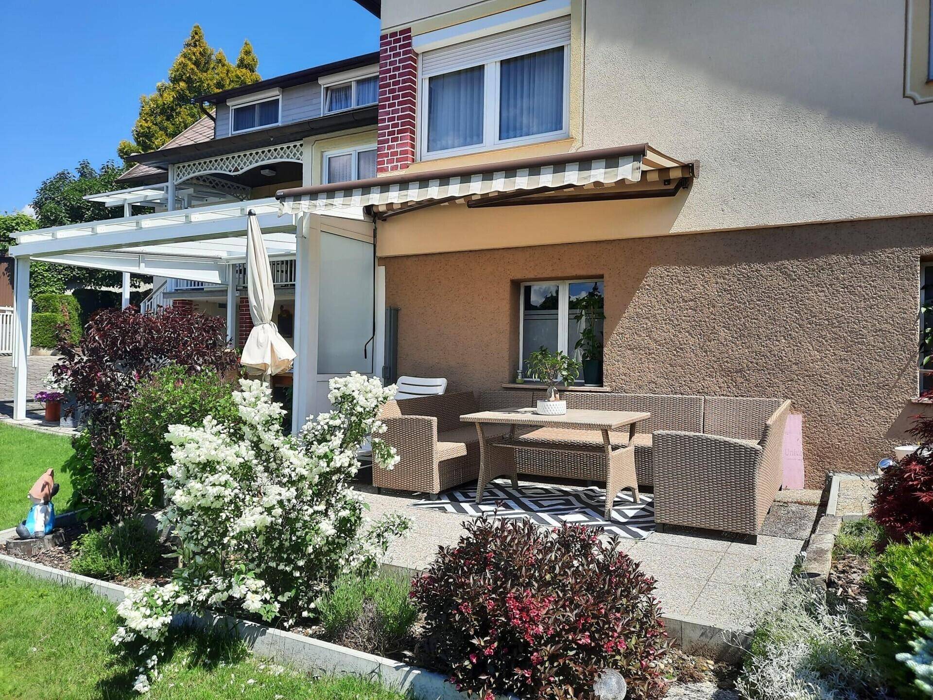 Gemütliche gepflasterte Terrasse mit Rattanmöbeln und ausziehbarer Markise für Schatten.