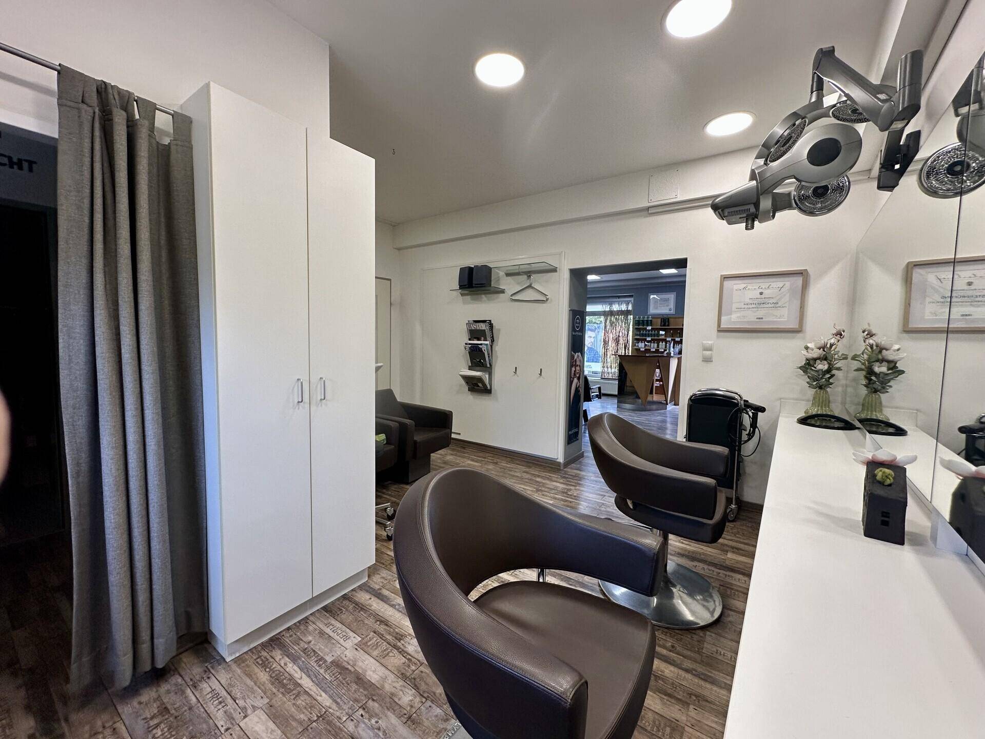 Styling-Bereich im Friseursalon mit modernen Stühlen, großen Spiegeln und weißen Schränken.