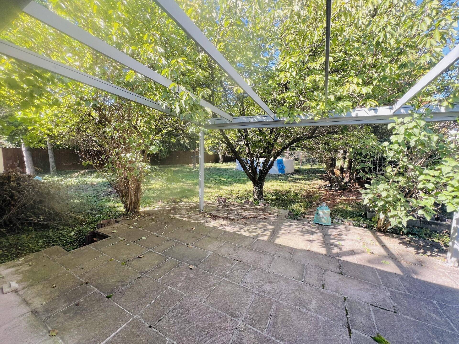 Gepflasterte Terrasse mit Überdachung und Blick in den grünen Garten.