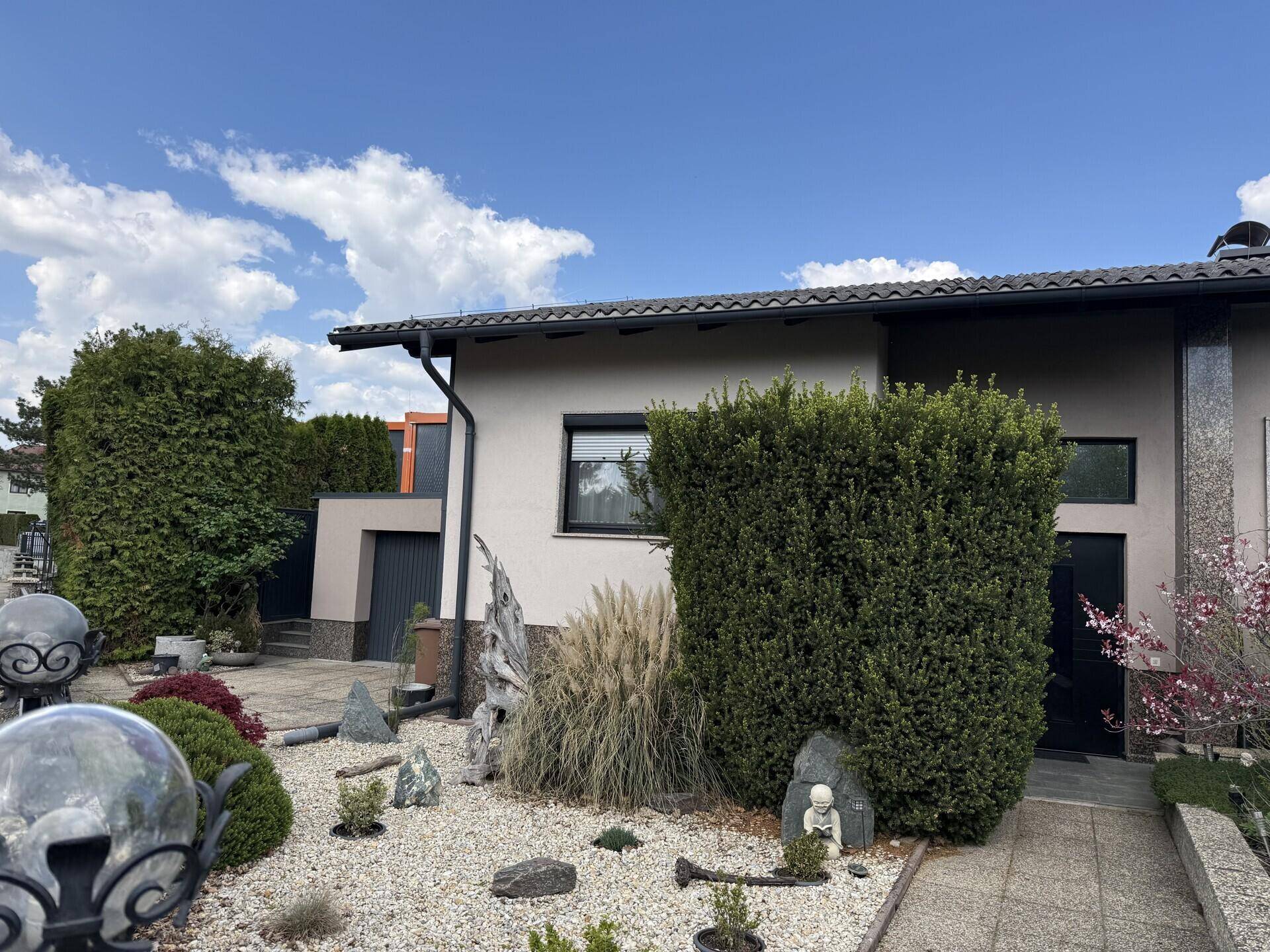 Vorderansicht des Hauses mit Eingangsbereich, Kiesgarten und hohen Hecken.