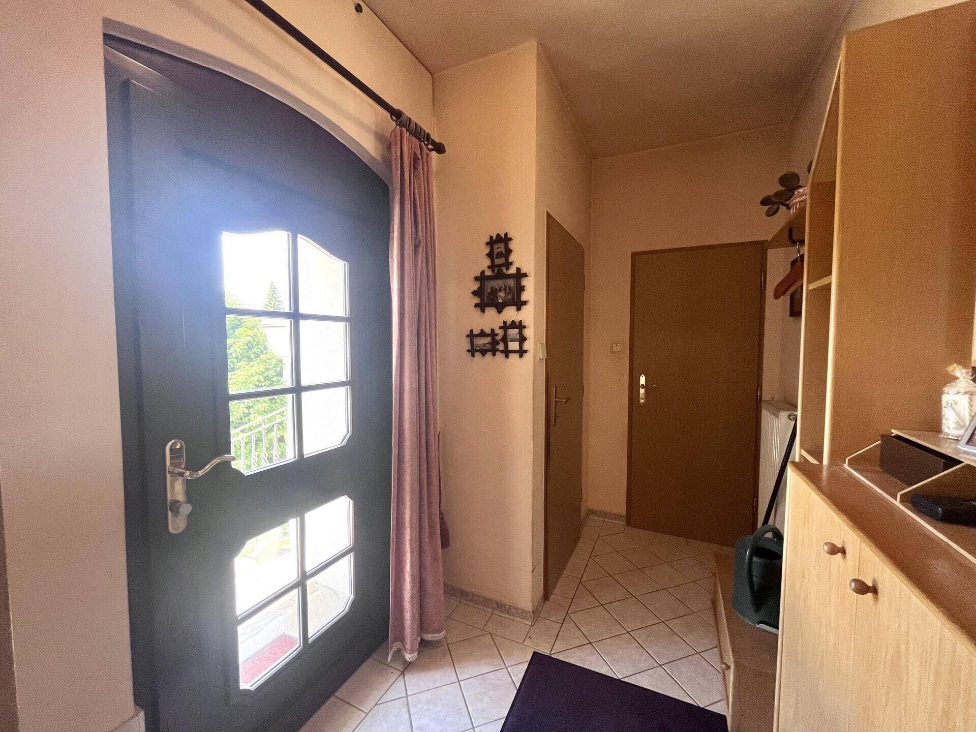 Heller Eingangsbereich mit gefliestem Boden, Haustür mit Glaseinsätzen und Garderobenmöbeln.